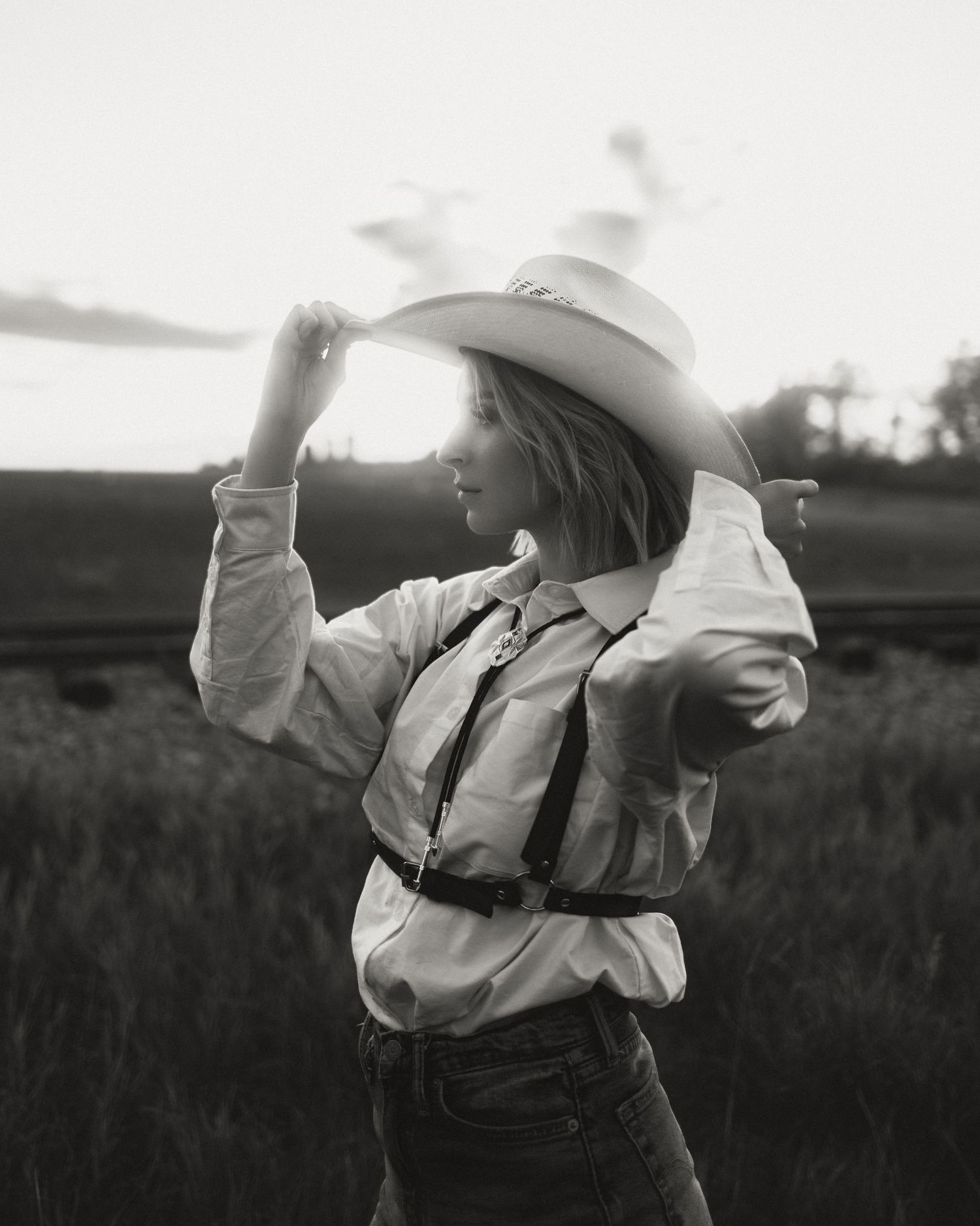 Figure in white shirt and cowboy hat dances in a field at sunset.