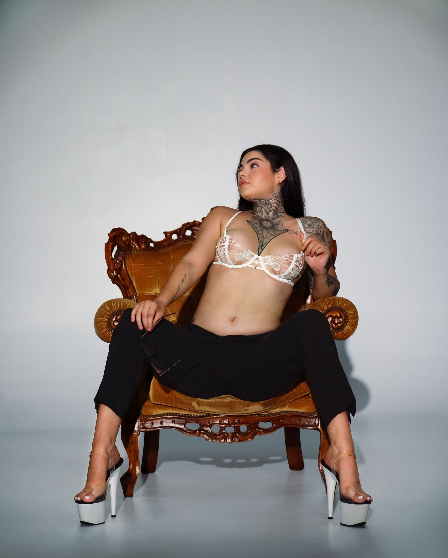 Figure lounges dramatically across ornate vintage chair in artistic black and white photo series.