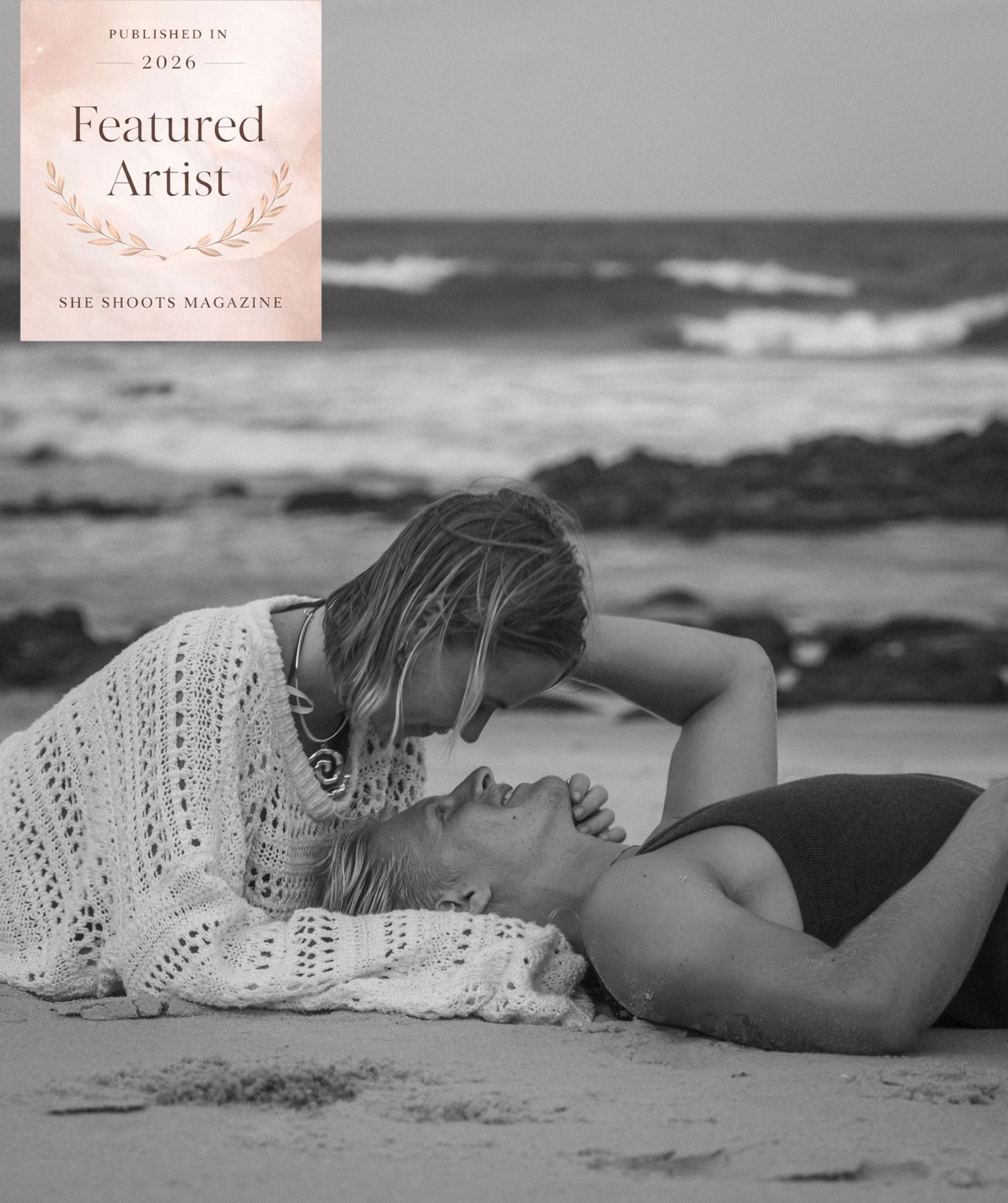 Black and white beach photo of two women sharing an intimate moment, featured in She Shoots Magazine 2026.