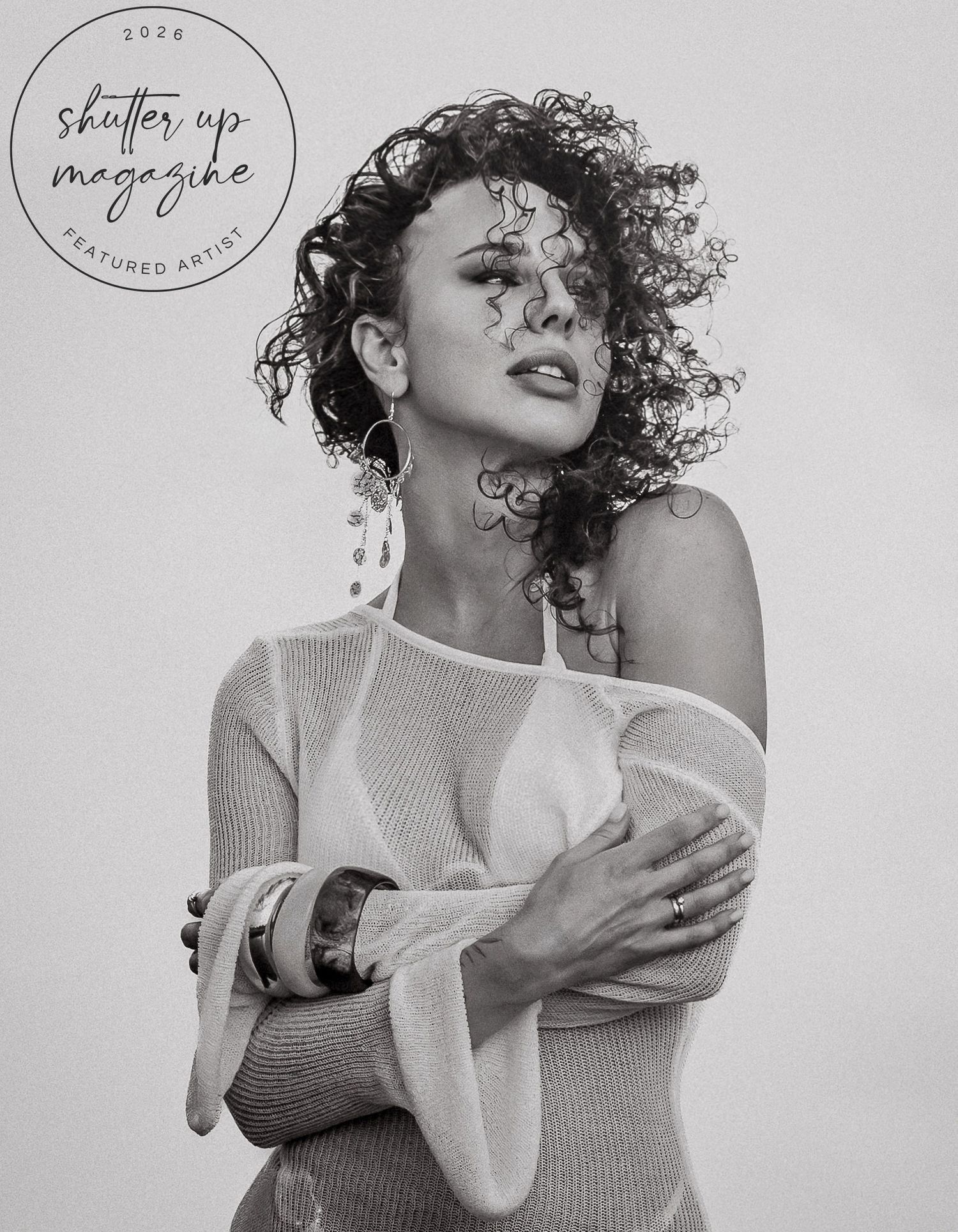 Black and white portrait of a curly-haired woman in off-shoulder top, featured in Shutter Up Magazine 2026.