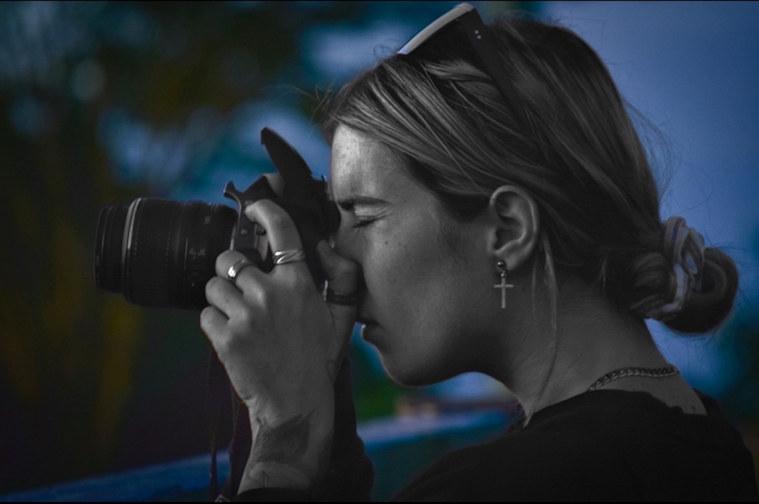 A photographer using a professional camera captured in black and white against blue sky.
