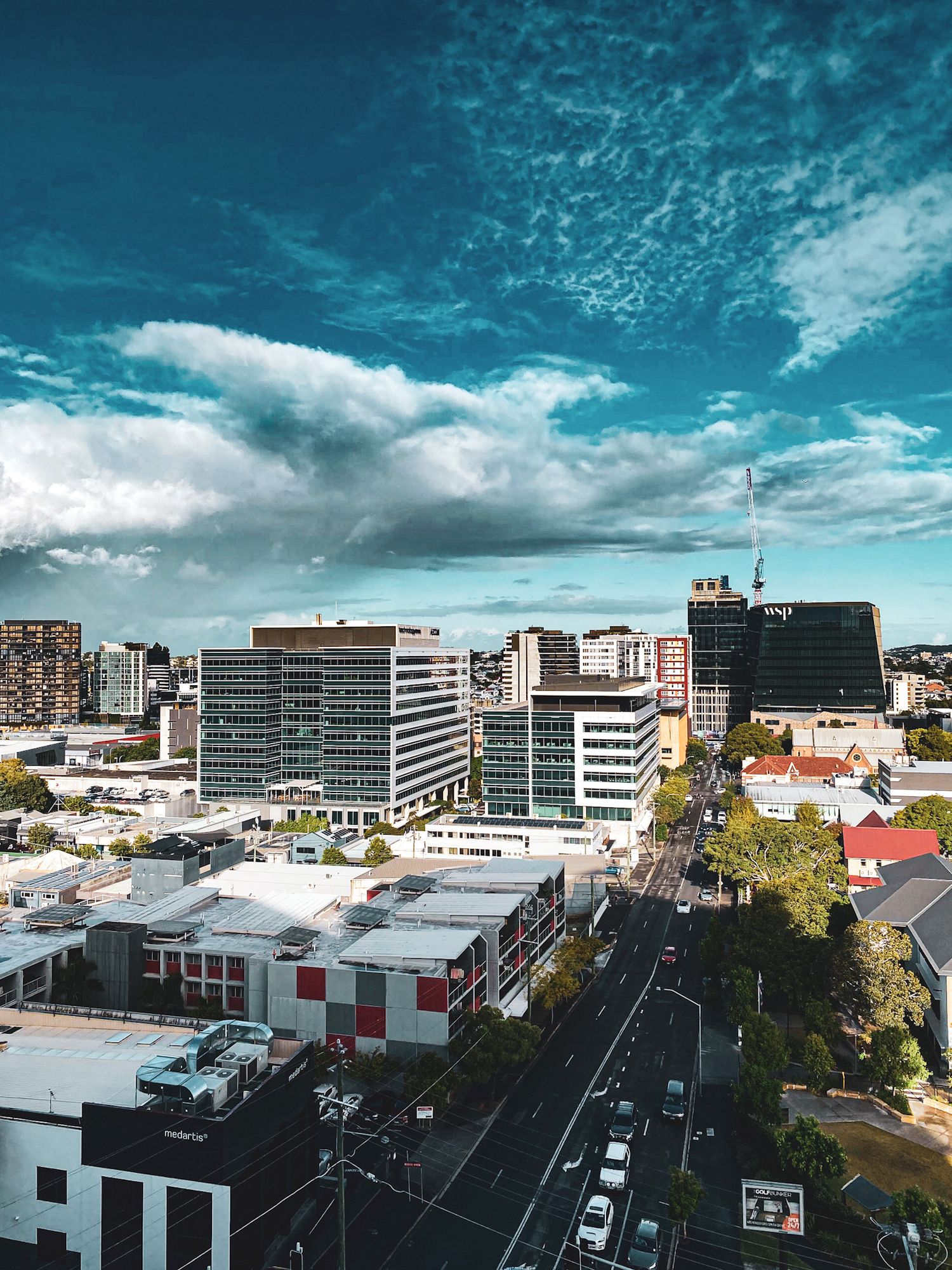 Aerial view of a bustling city skyline with modern buildings, tree-lined streets, and a dramatic blue sky with clouds.