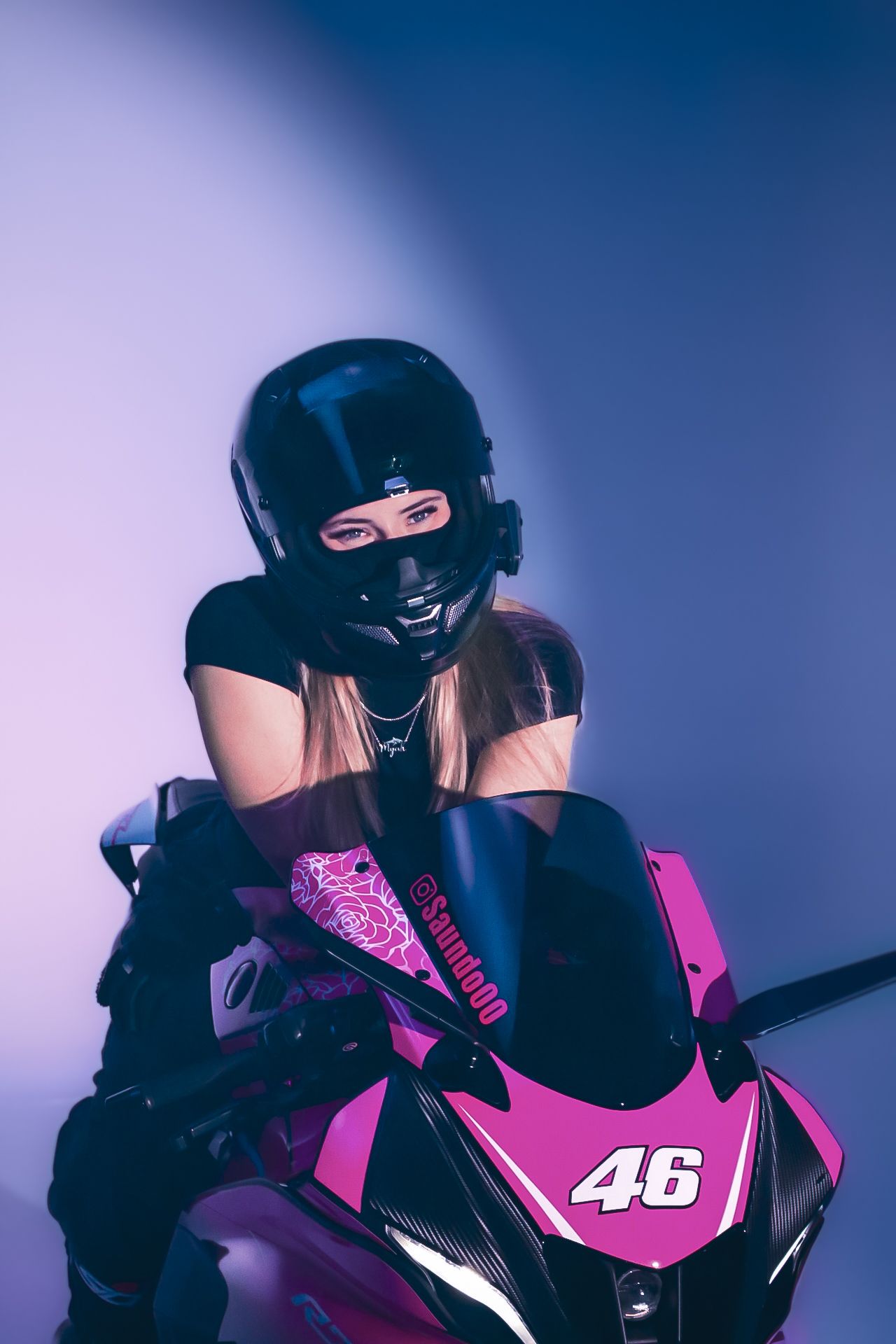 Pink and black sports motorcycle with rider against purple backdrop.