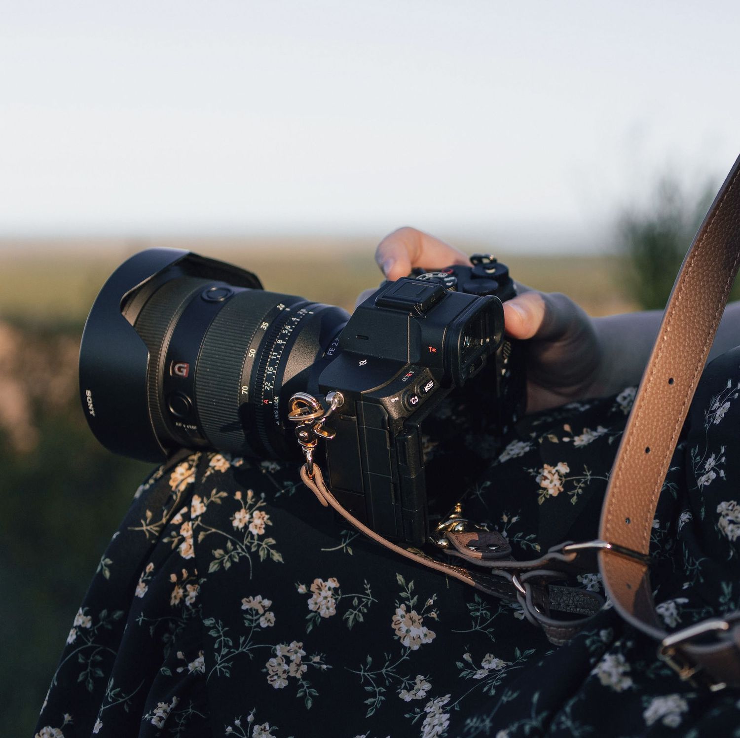 Close-up sequence of a camera lens with floral patterned strap against blurred outdoor background.