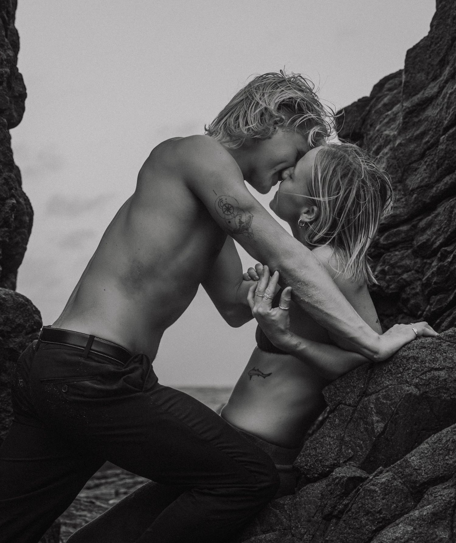 A black and white photo sequence showing a couple embracing and climbing on coastal rocks.