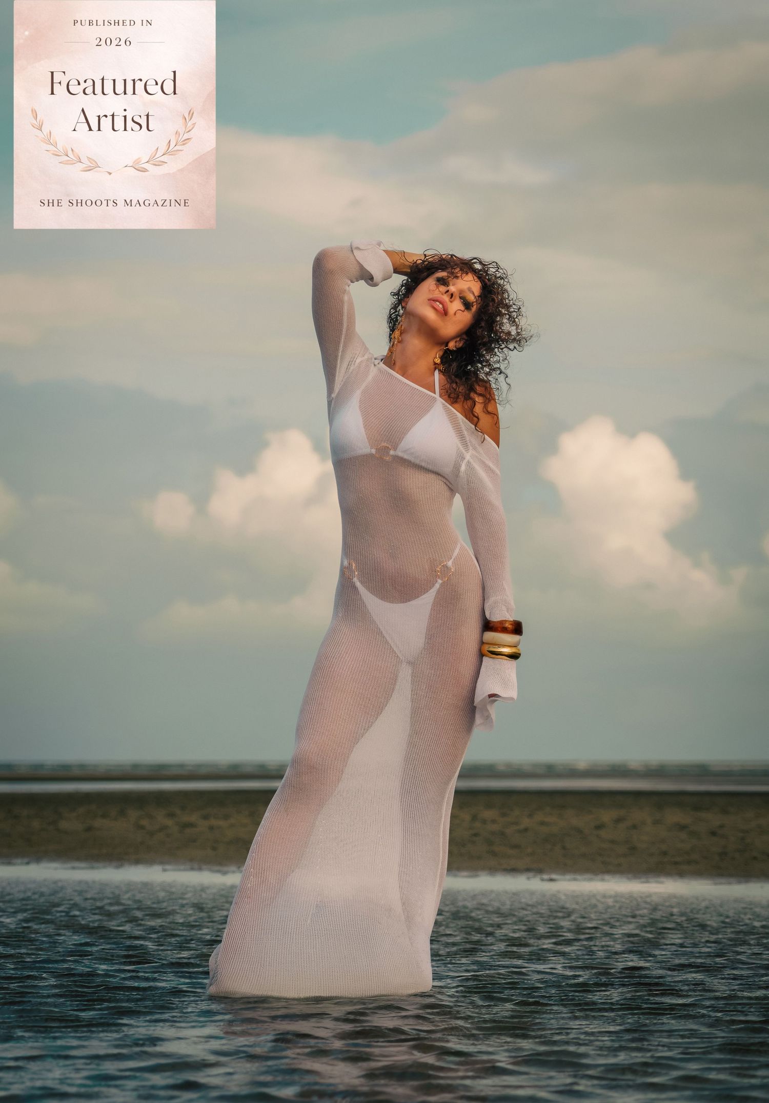 Woman in white sheer mesh dress stands in shallow ocean water, featured in She Shoots Magazine 2024.