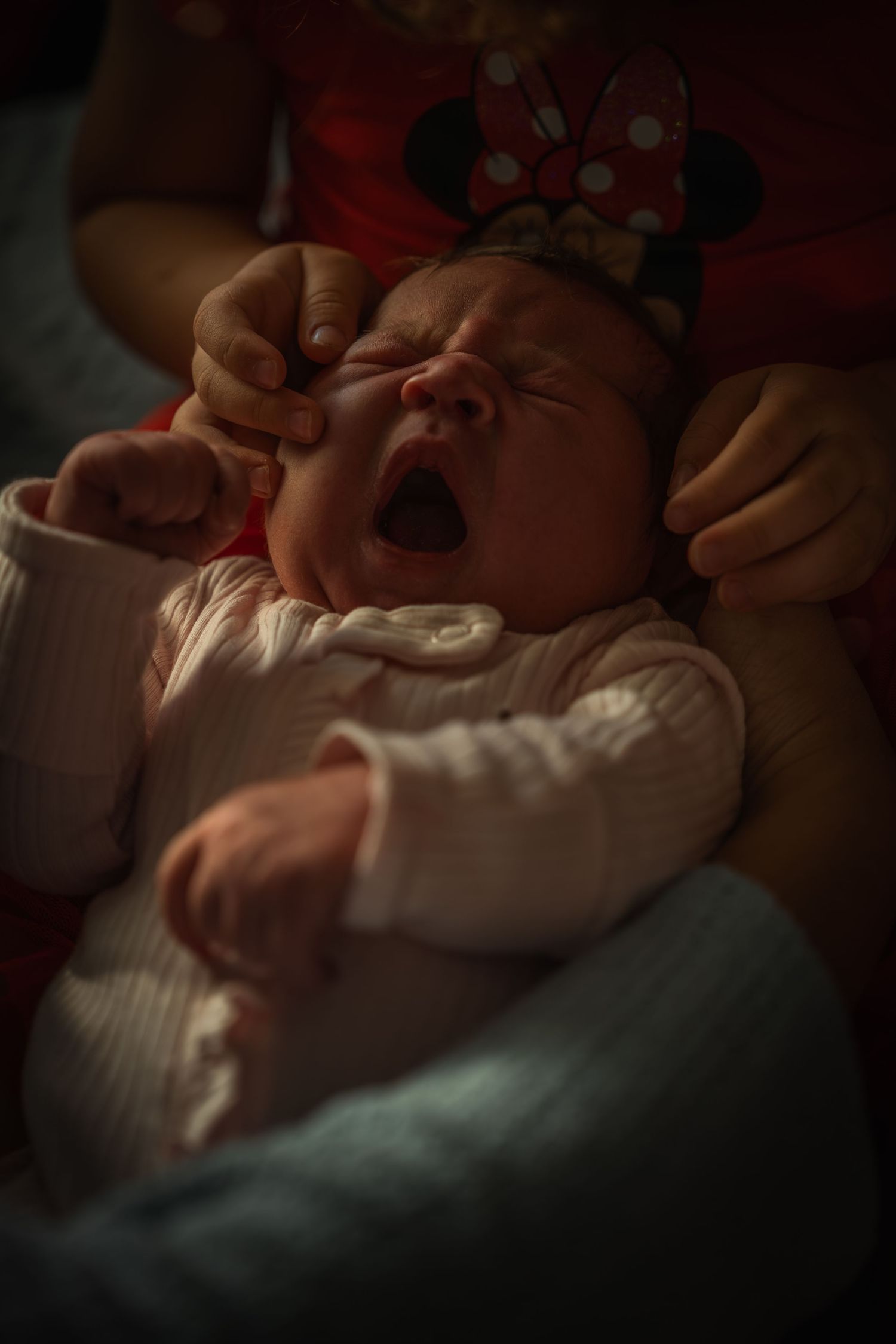 Yawning baby wearing a white outfit being cradled.