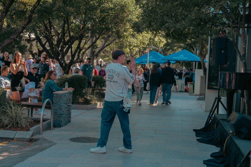 People gathering at an outdoor event with trees and tents visible.