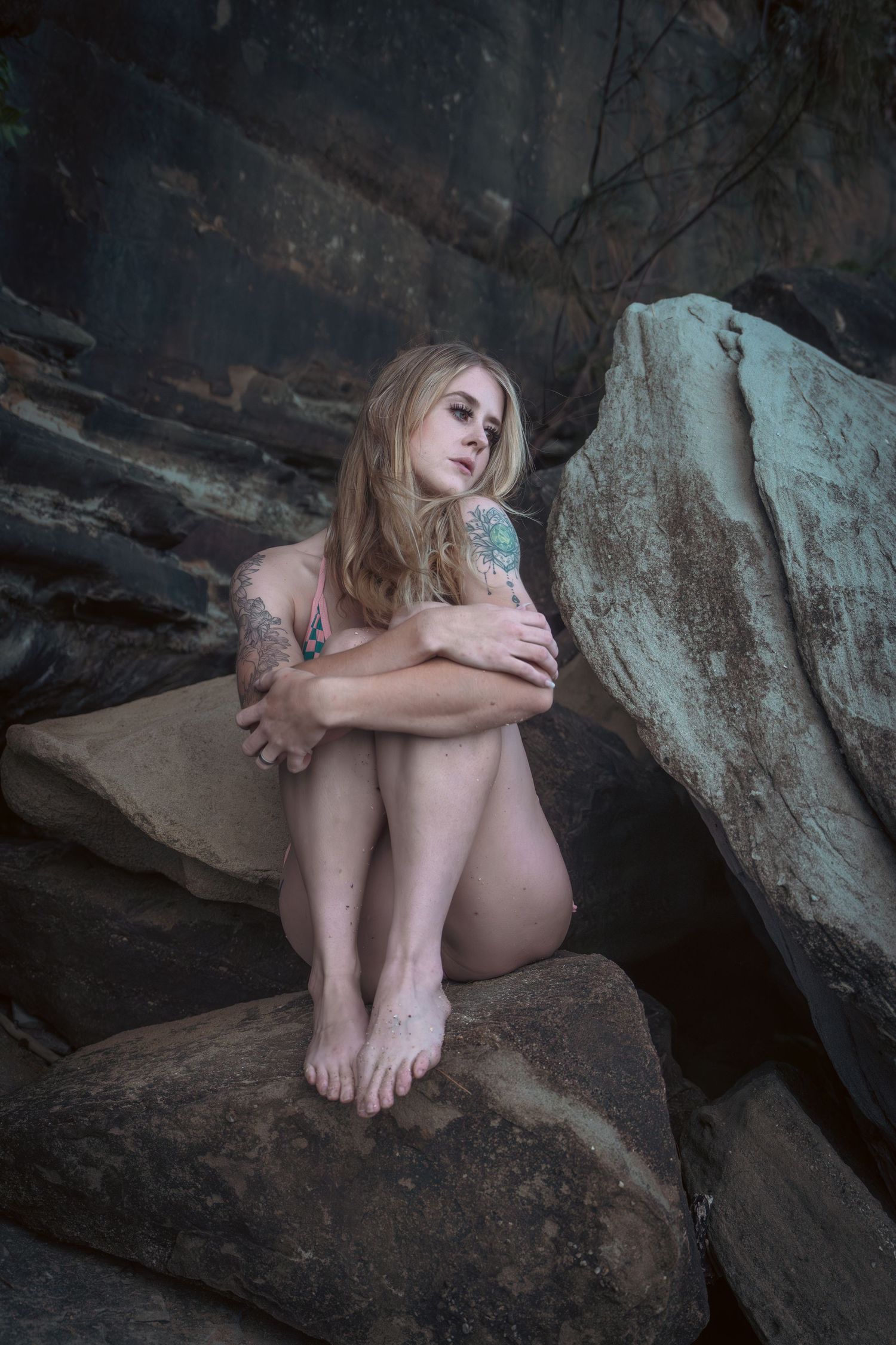 Intimate portrait showing a model resting on stone formations in a cave setting.
