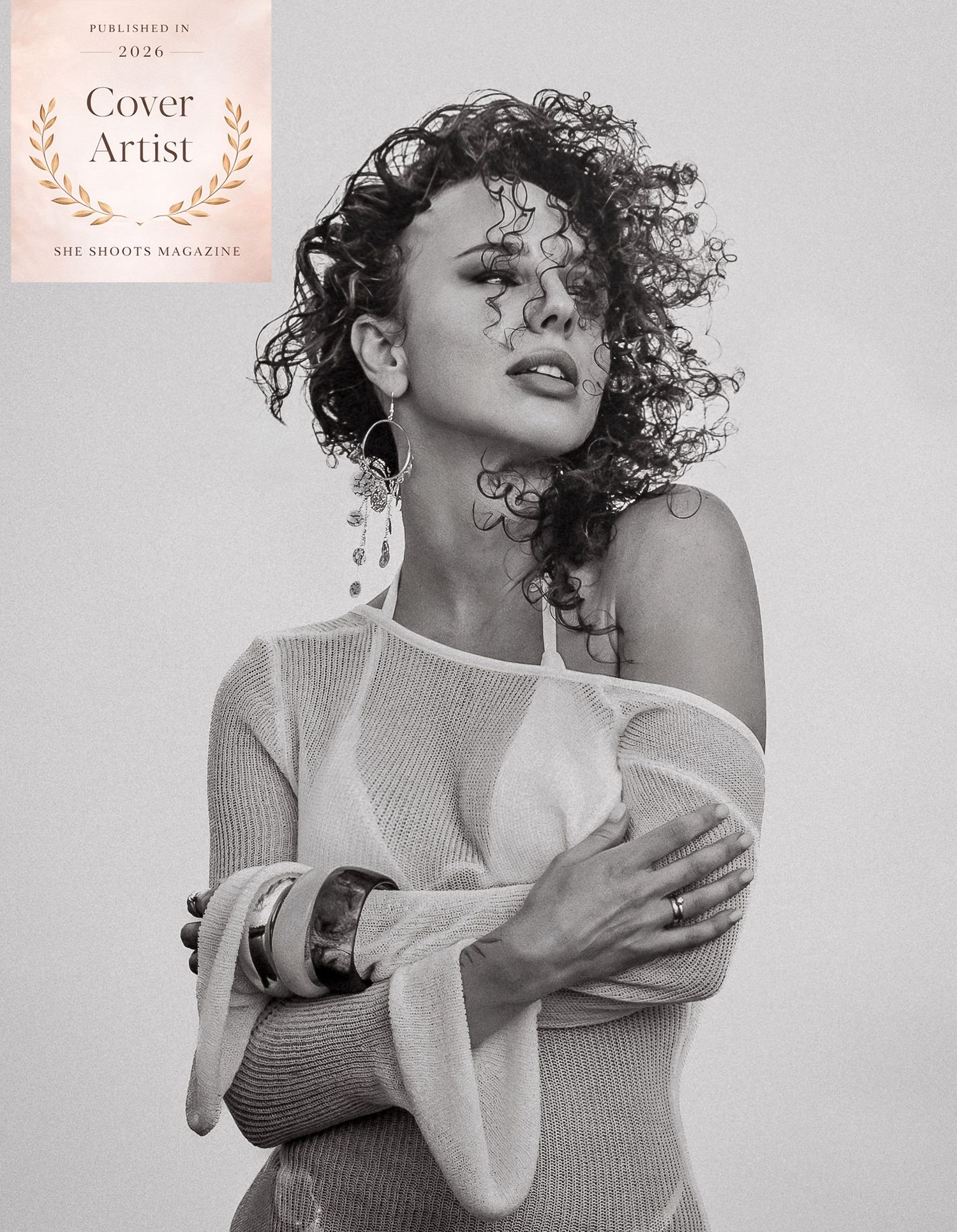 Black and white portrait of a curly-haired woman in off-shoulder top, featured as She Shoots Magazine Cover Artist 2026.
