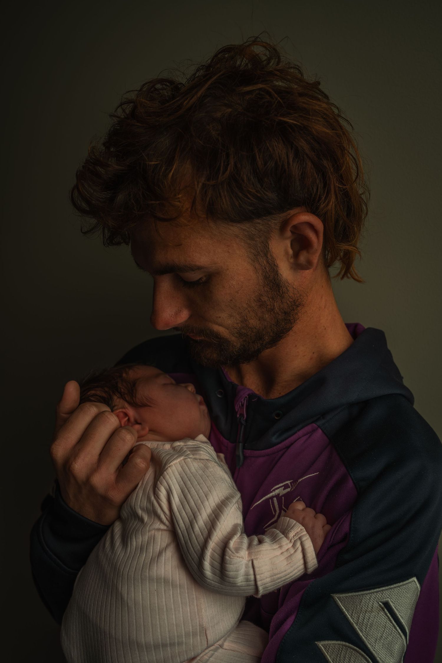 Intimate moment between parent and newborn in moody lighting.