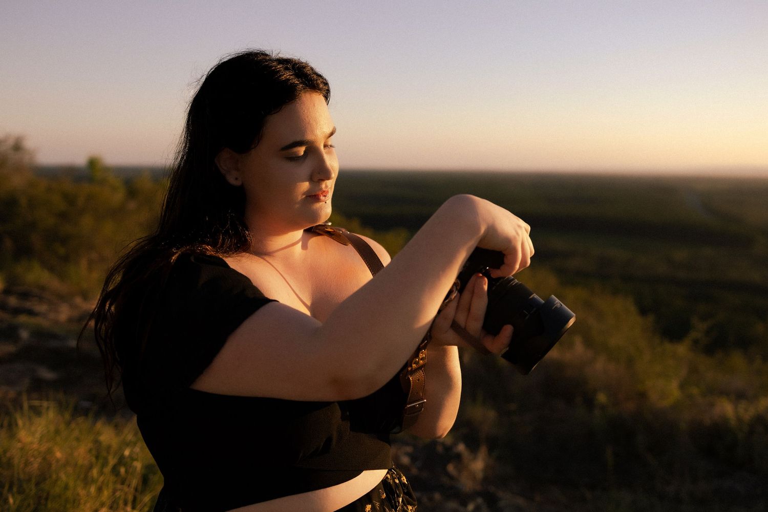 Sunshine Coast Photographer Woman photographer reviewing camera settings outdoors at golden hour with scenic landscape in background.
