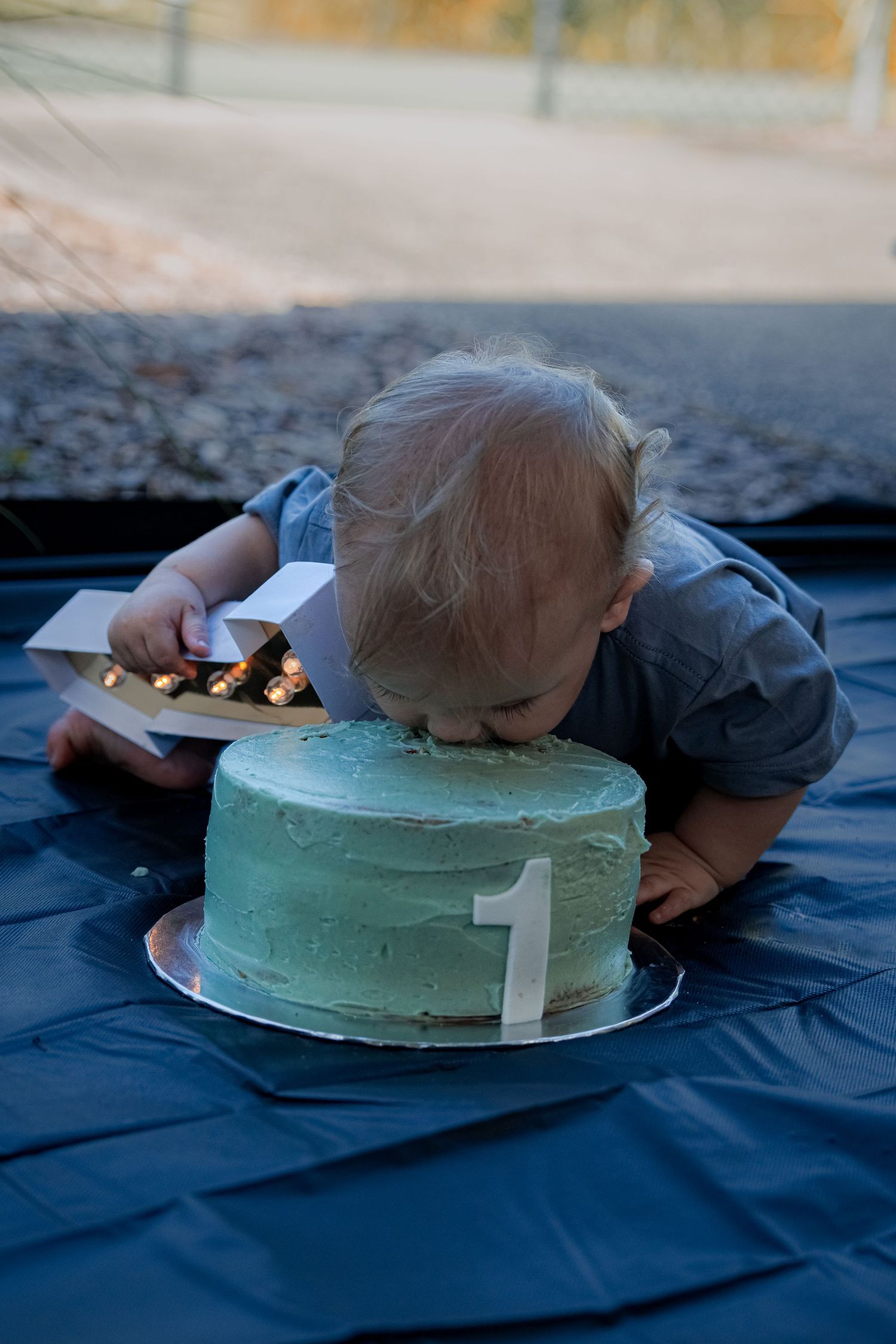 A light blue birthday cake with white decorations on a dark blue tablecloth.