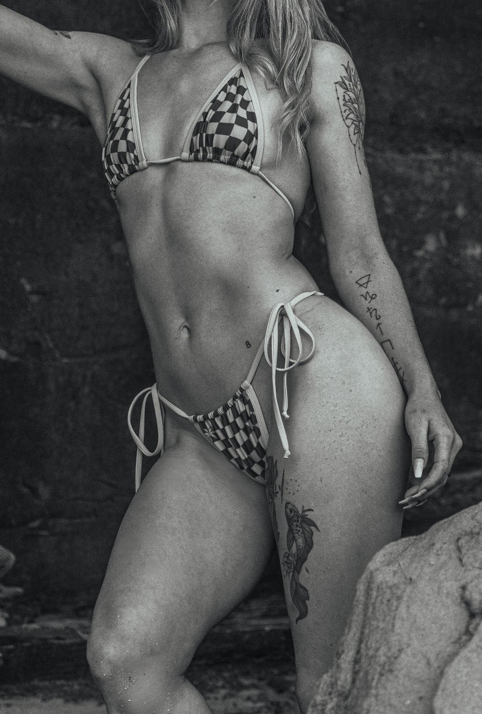 Black and white beach photoshoot featuring a checkered bikini and natural poses on rocks.
