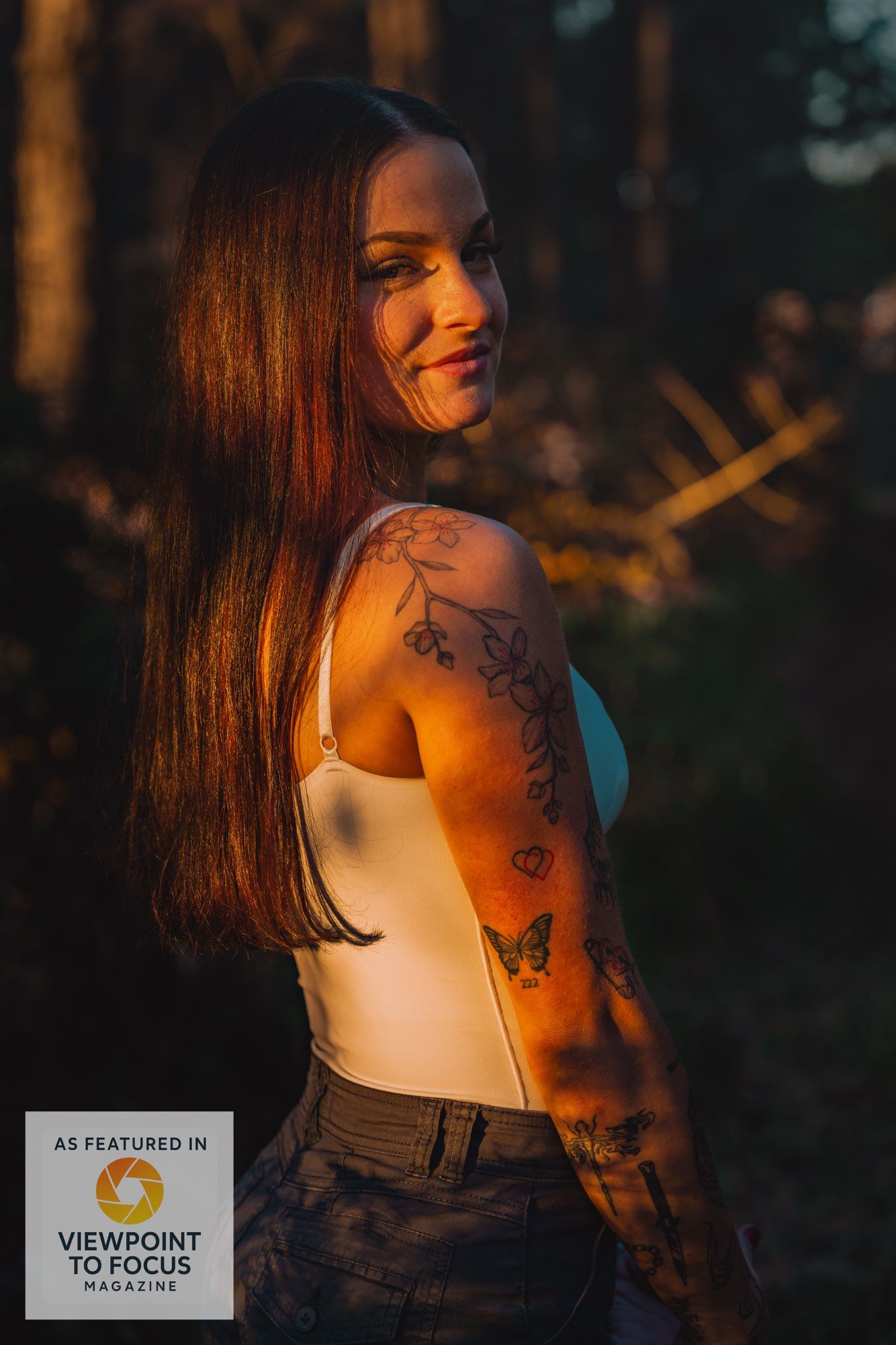 Portrait of a woman with tattoos in a forest during golden hour with warm sunset lighting.