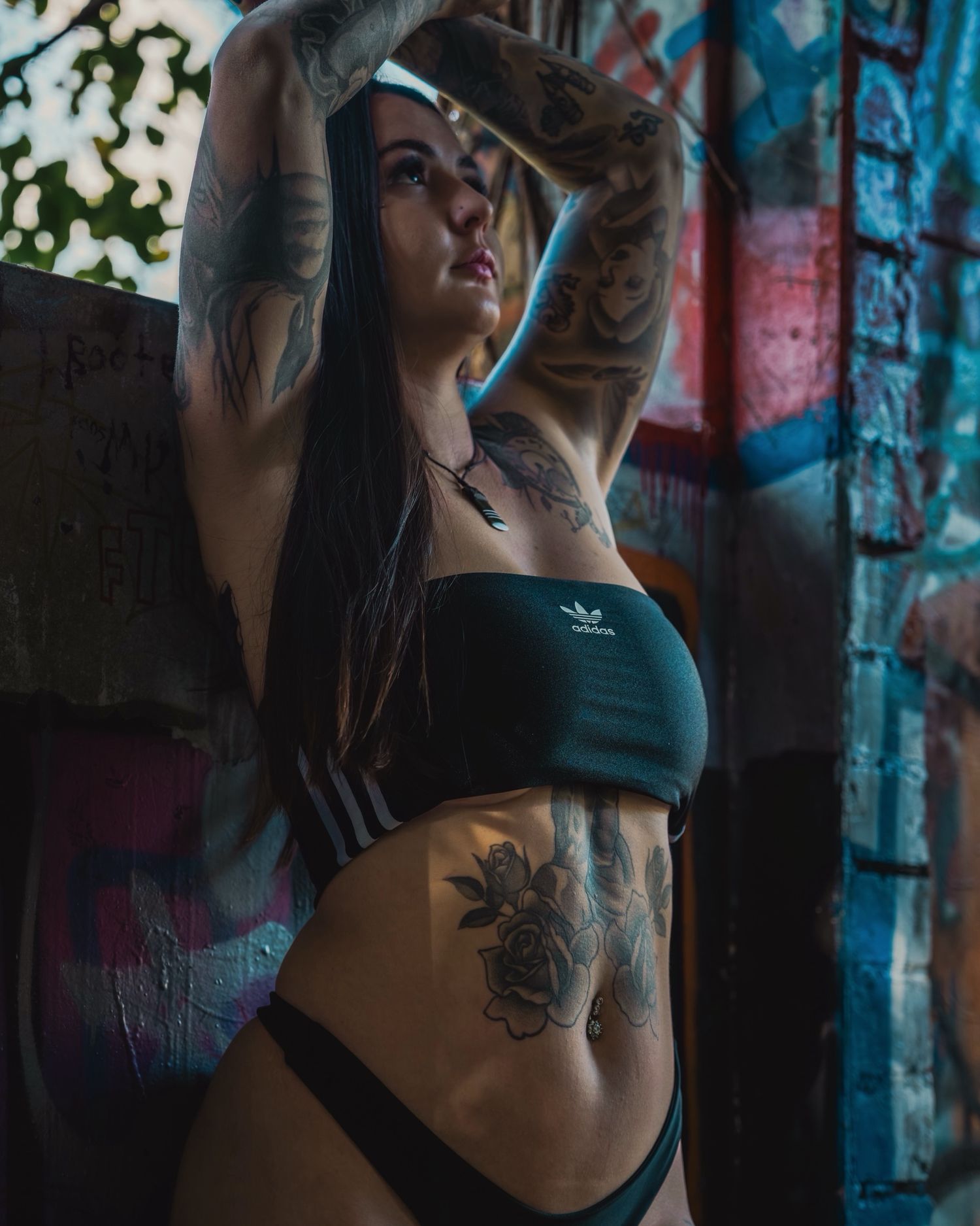 A tattooed person in athletic wear poses against colorful graffiti wall.