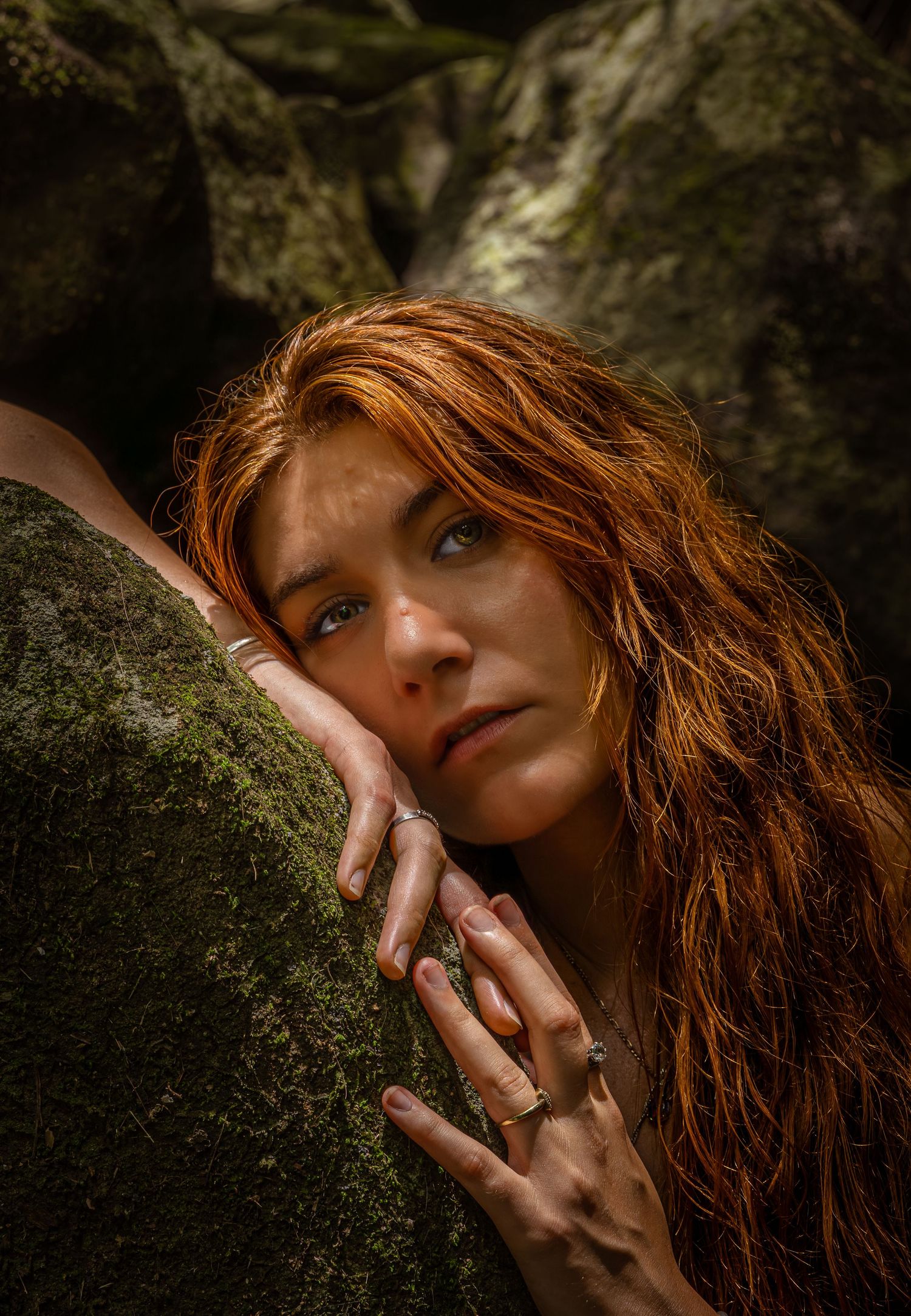 Artistic portrait series showing red hair against dark mossy rocks in dramatic lighting and shadows.