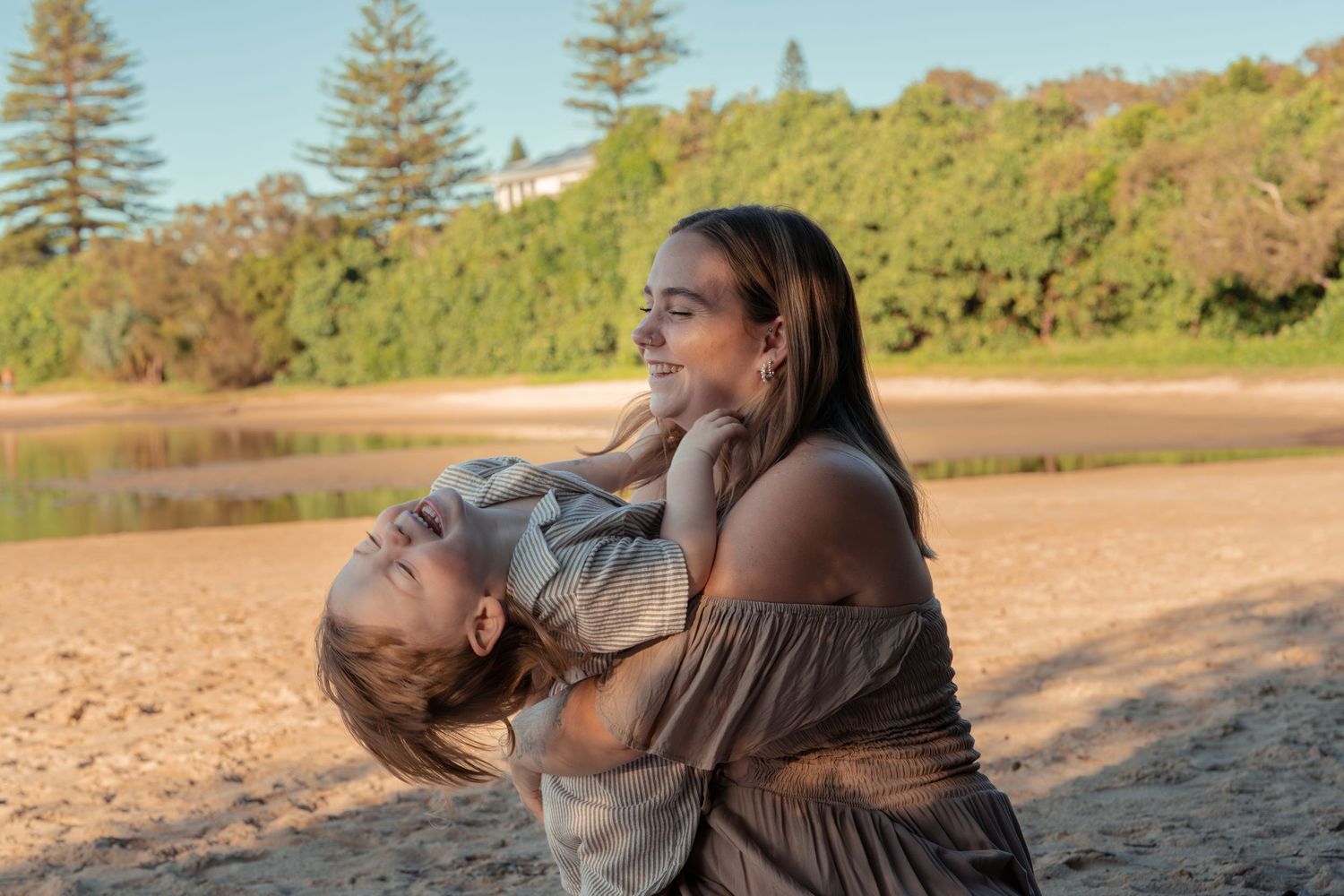 Parent and child sharing playful moment on sandy beach.