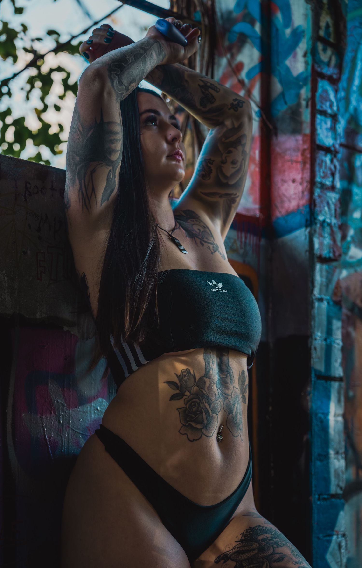 Athletic figure in dark sportswear poses against graffiti wall showing tattoo art.