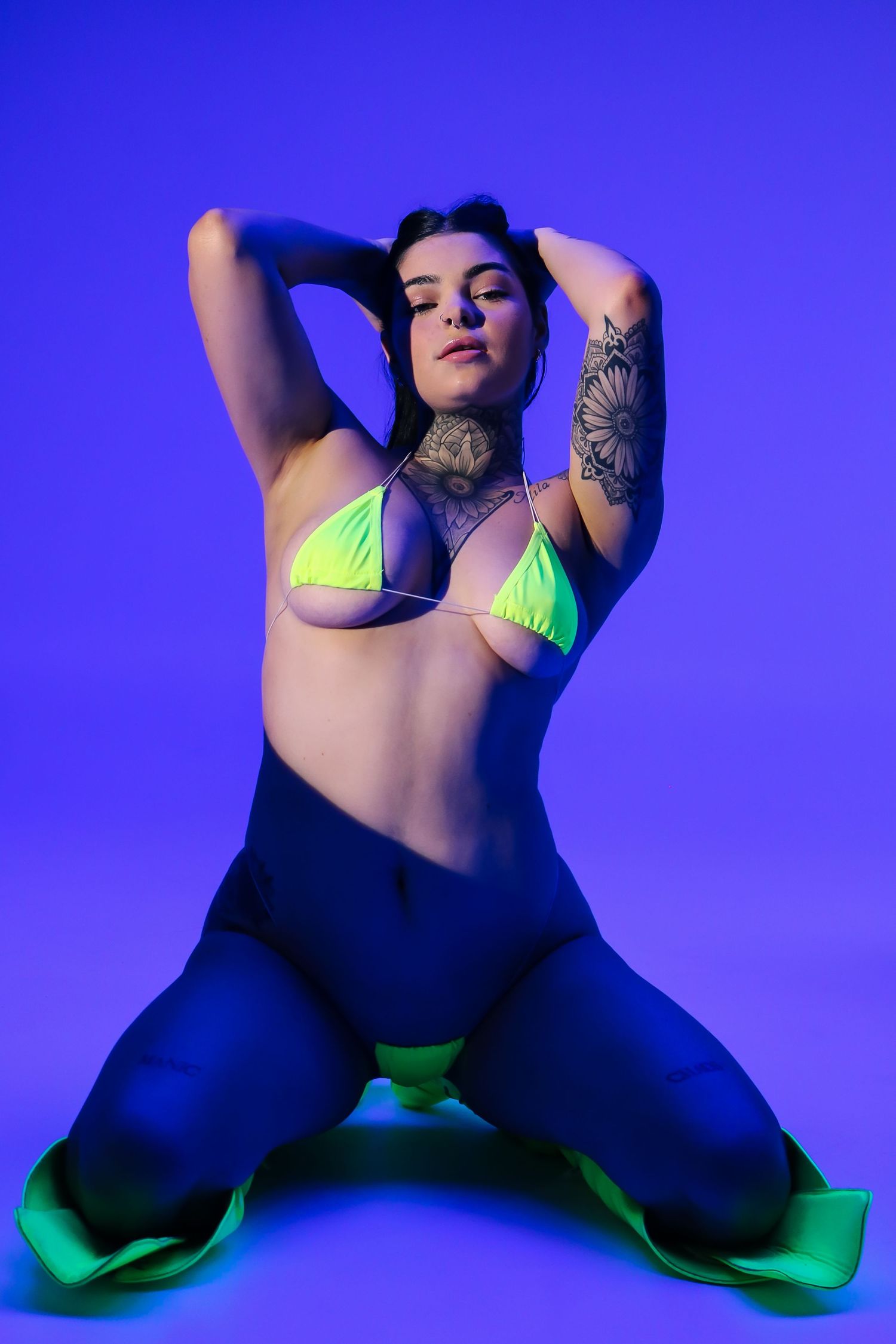 Model in neon green attire poses dramatically against blue background.