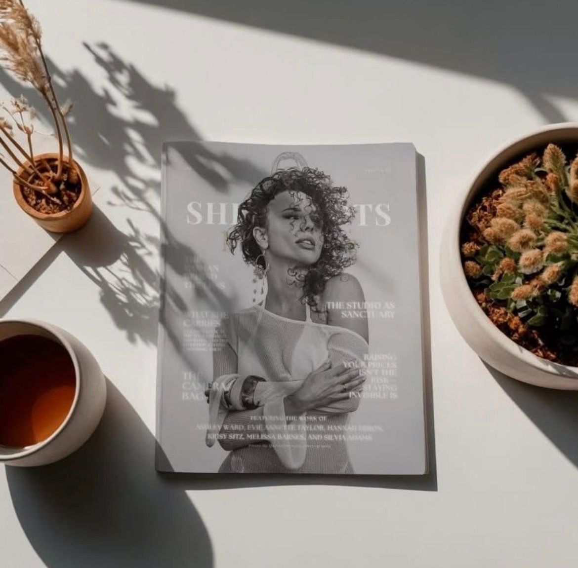 A Silhouettes magazine laid flat on a white surface beside a bowl of salad, a cup of tea, and a small plant.
