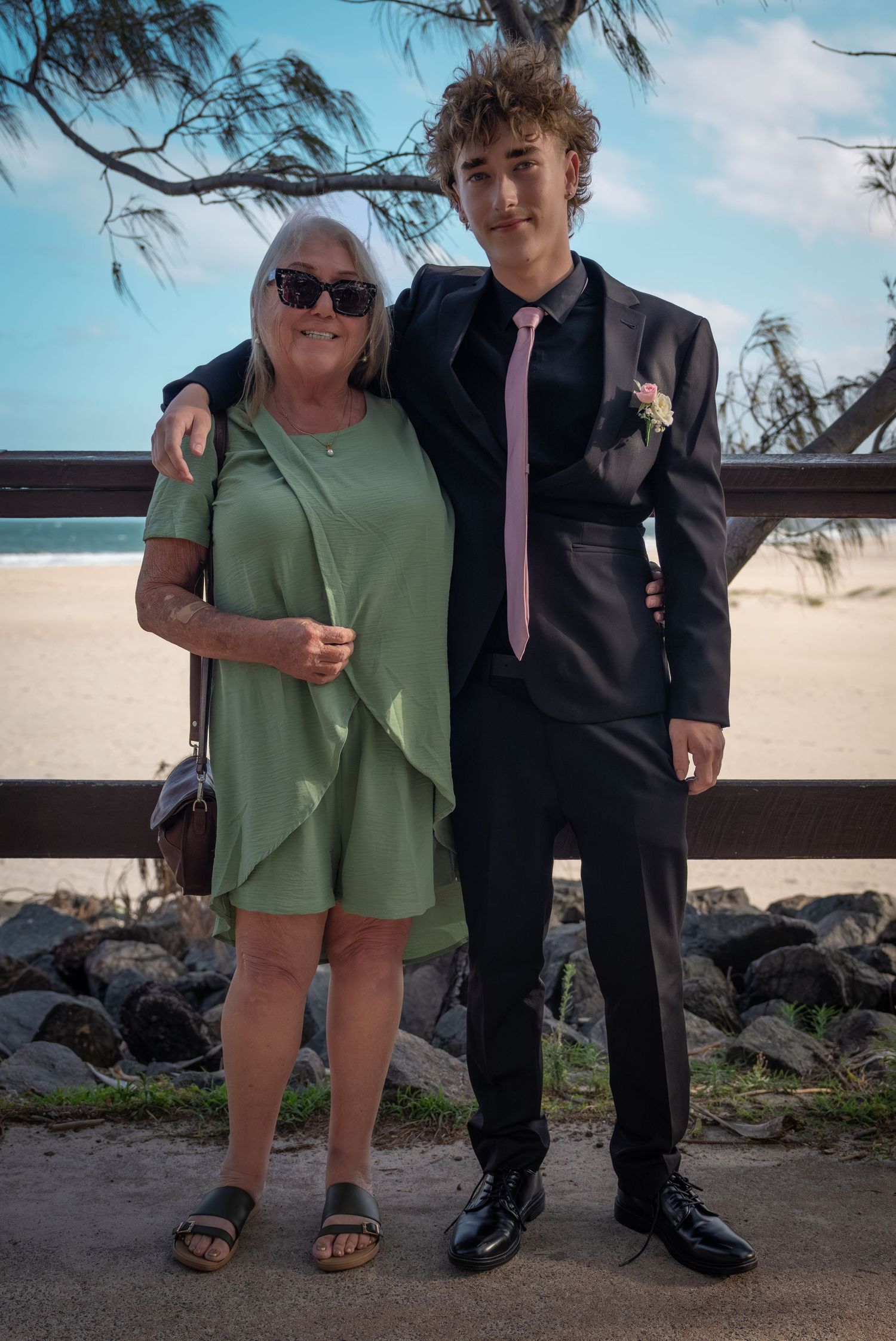 A beach scene with people in formal attire standing near rocky coastline.