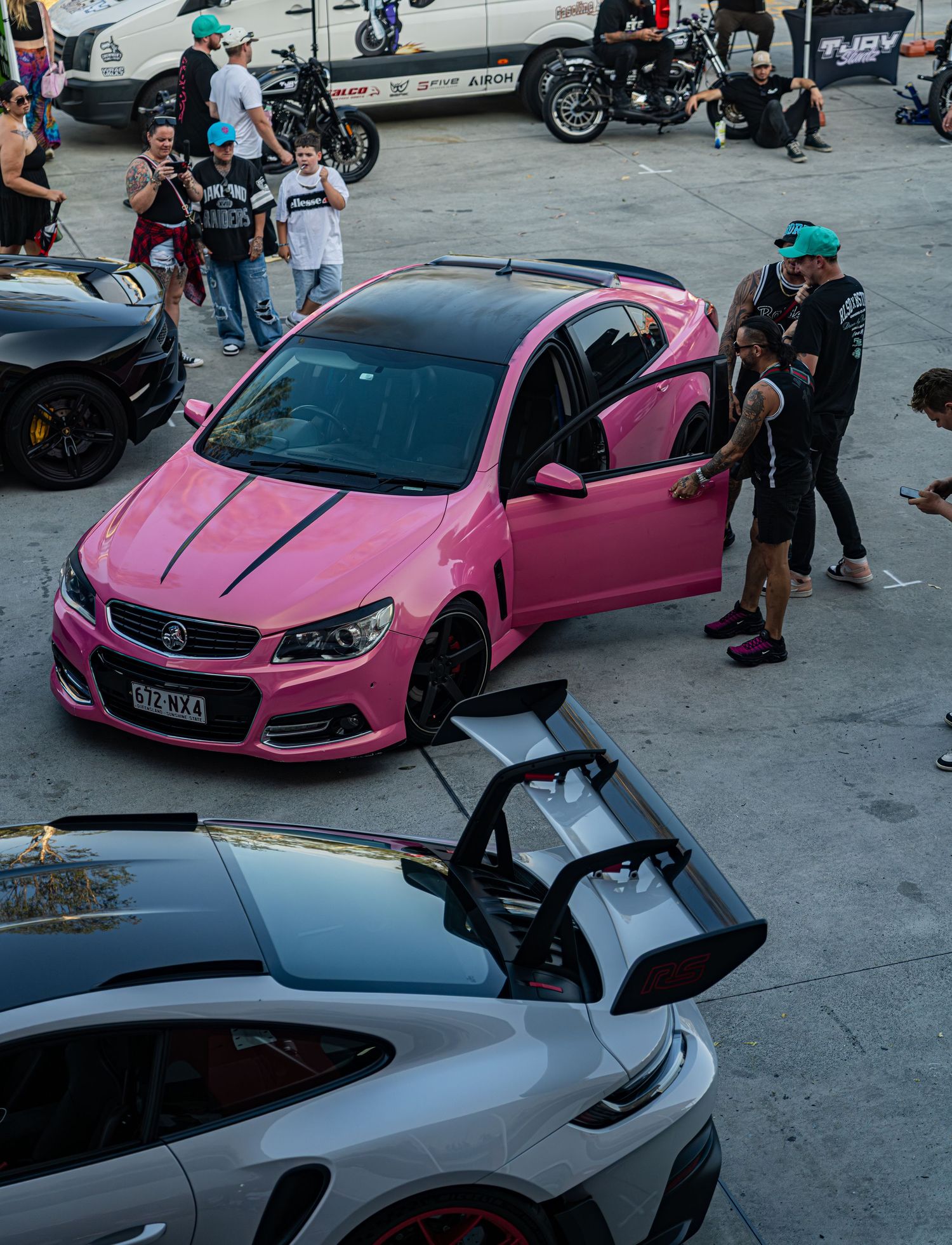Custom modified sports cars in pink and silver with scissor doors displayed at a car meet.