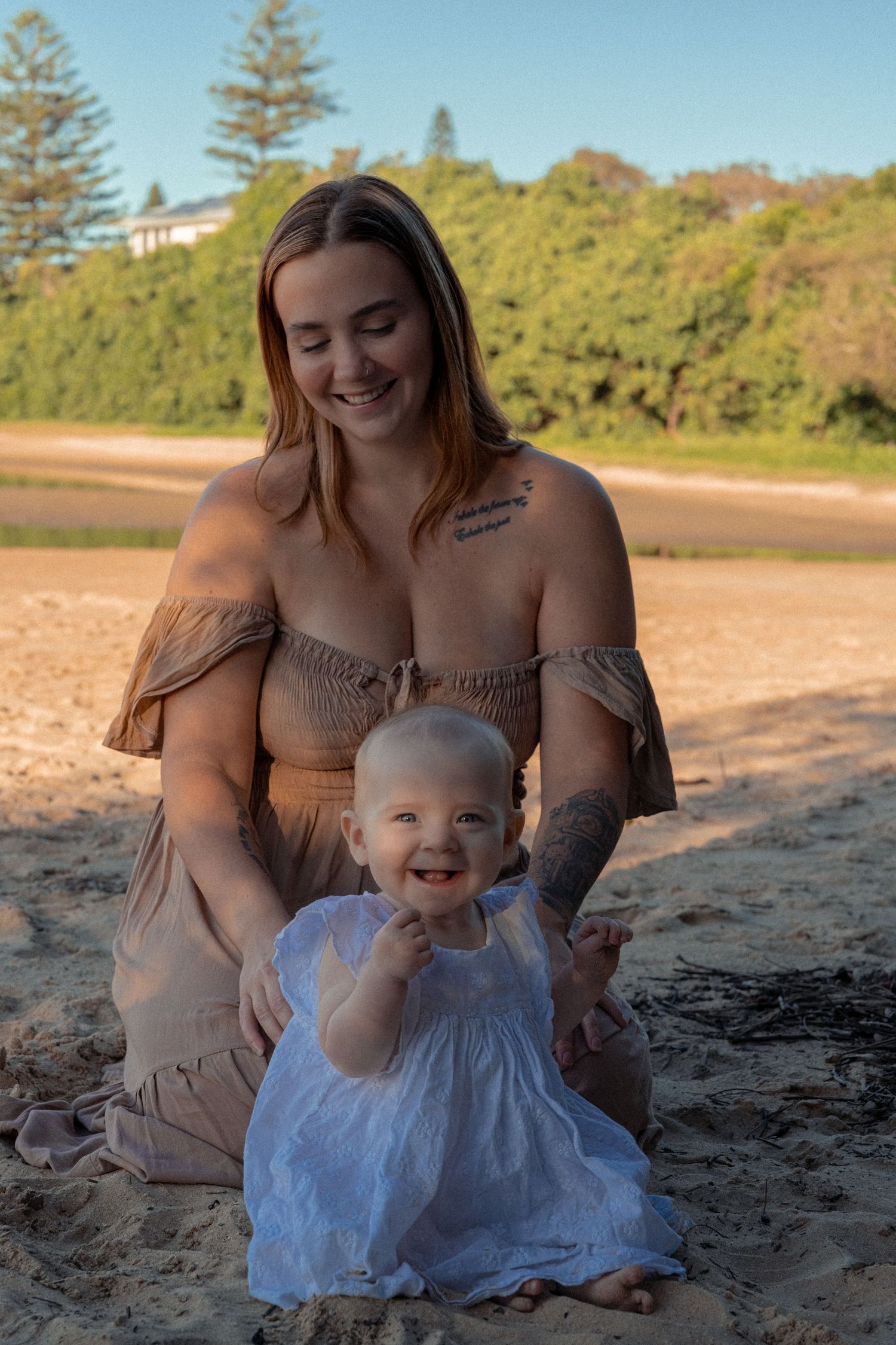 A heartwarming beach scene with a baby in a white dress playing in the sand at sunset.