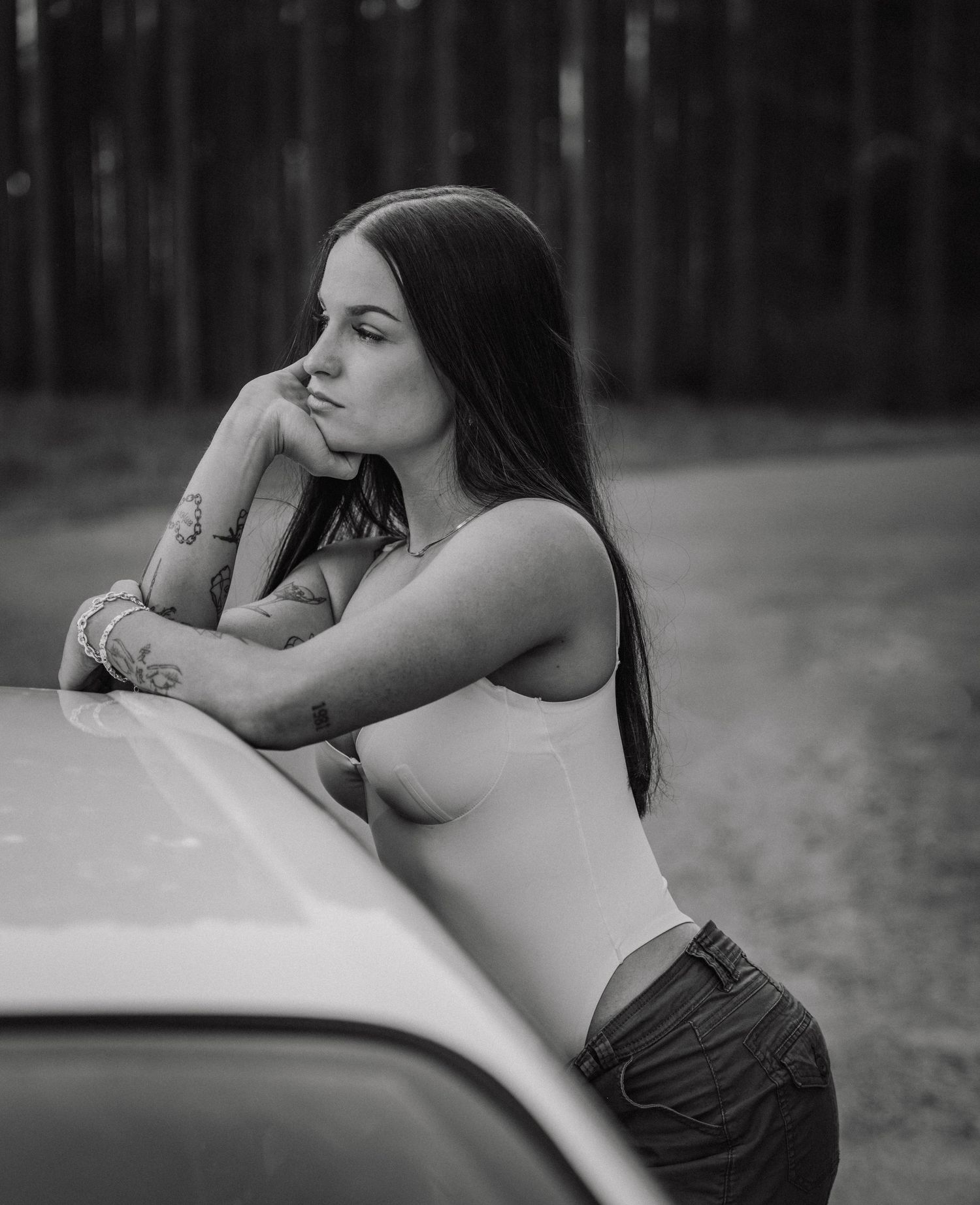 Black and white portrait of a model leaning against a car hood.