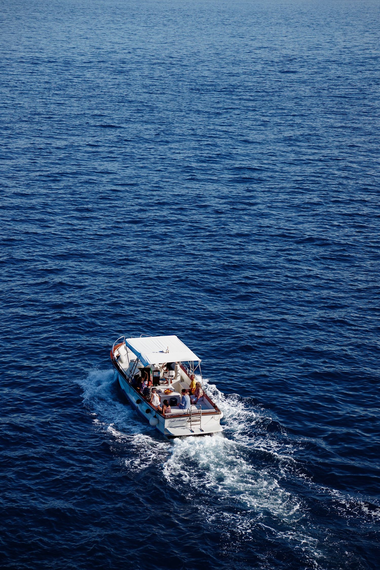 Small white motorboat cruising across deep blue Mediterranean waters.