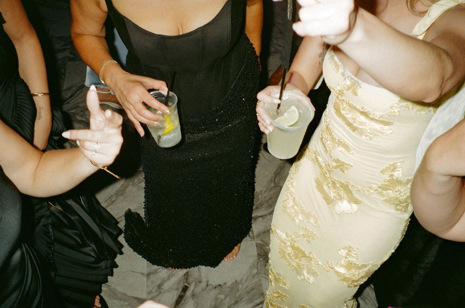 Three women in elegant dresses holding green cocktail drinks at a party event.