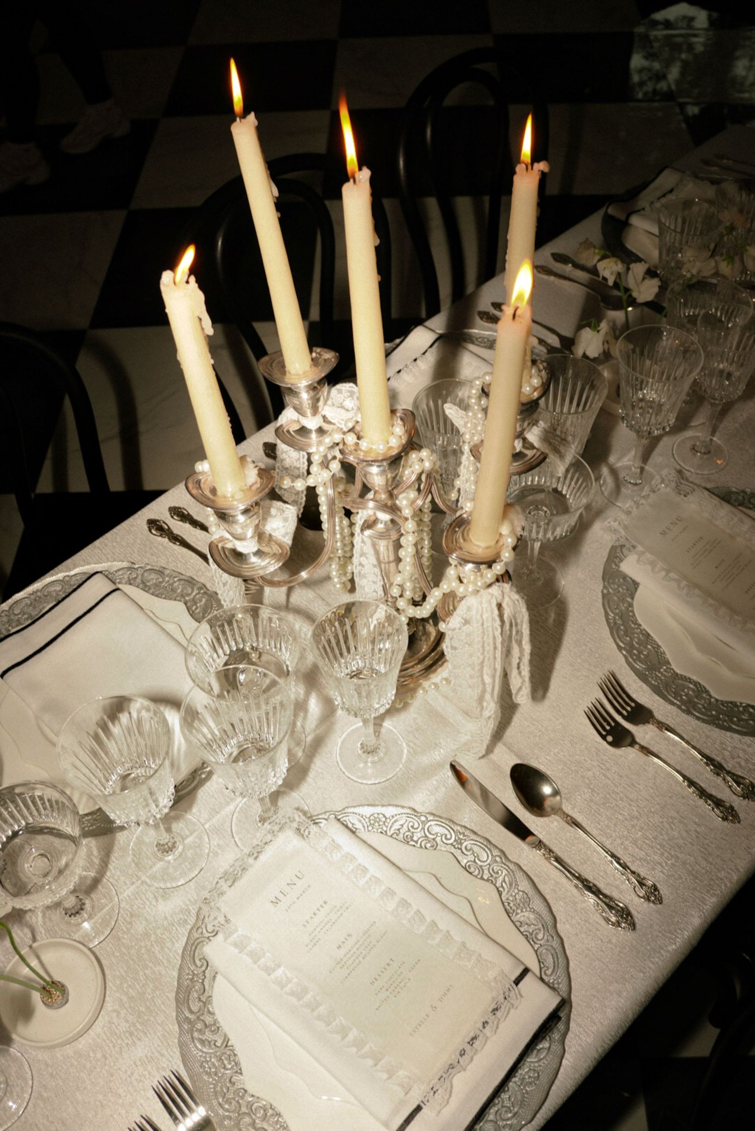Elegant candlelit dinner table with crystal candelabra, fine silverware, ornate plates, and glassware on a white tablecloth.