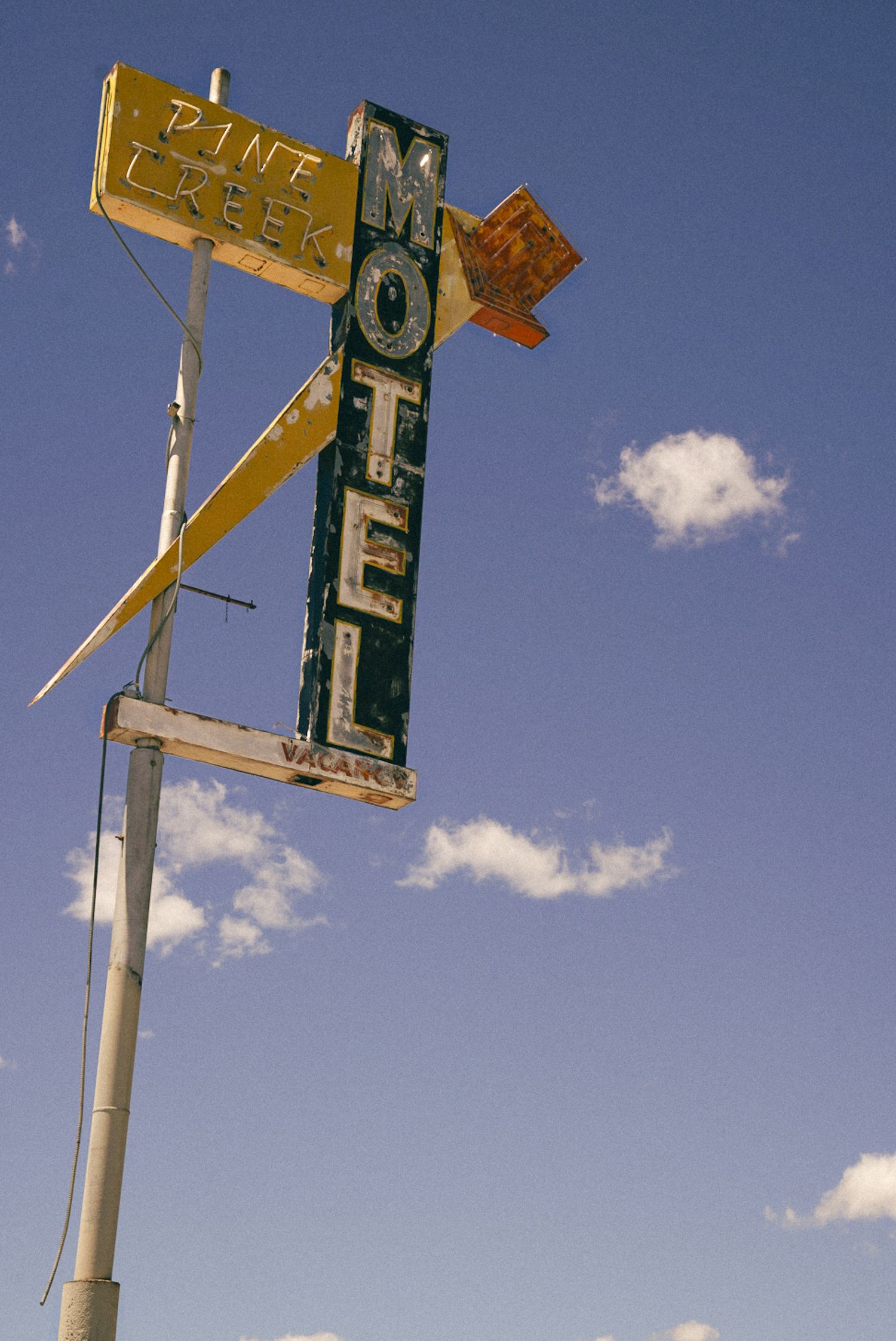 Vintage Pine Creek Motel neon sign on a tall pole against a blue sky with scattered clouds.
