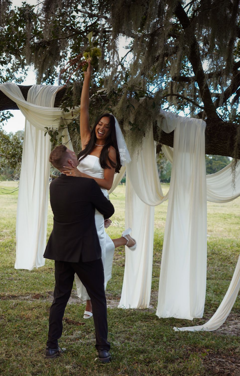 Couple dancing between white fabric drapes hung from trees in an outdoor setting.