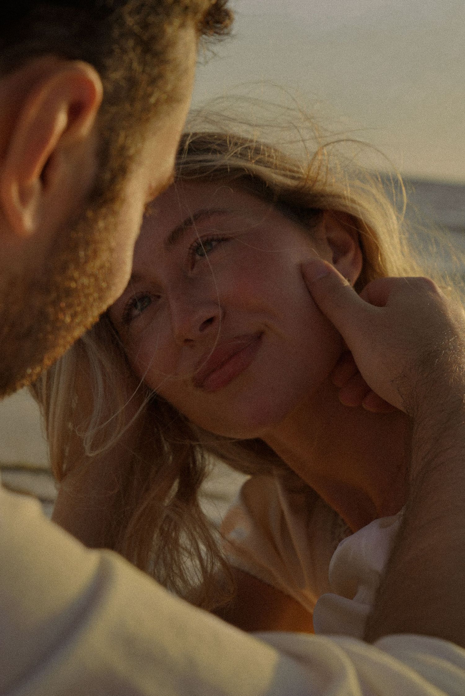 A couple shares a tender romantic moment at sunset on a beach, with a man gently cradling a smiling woman's face.