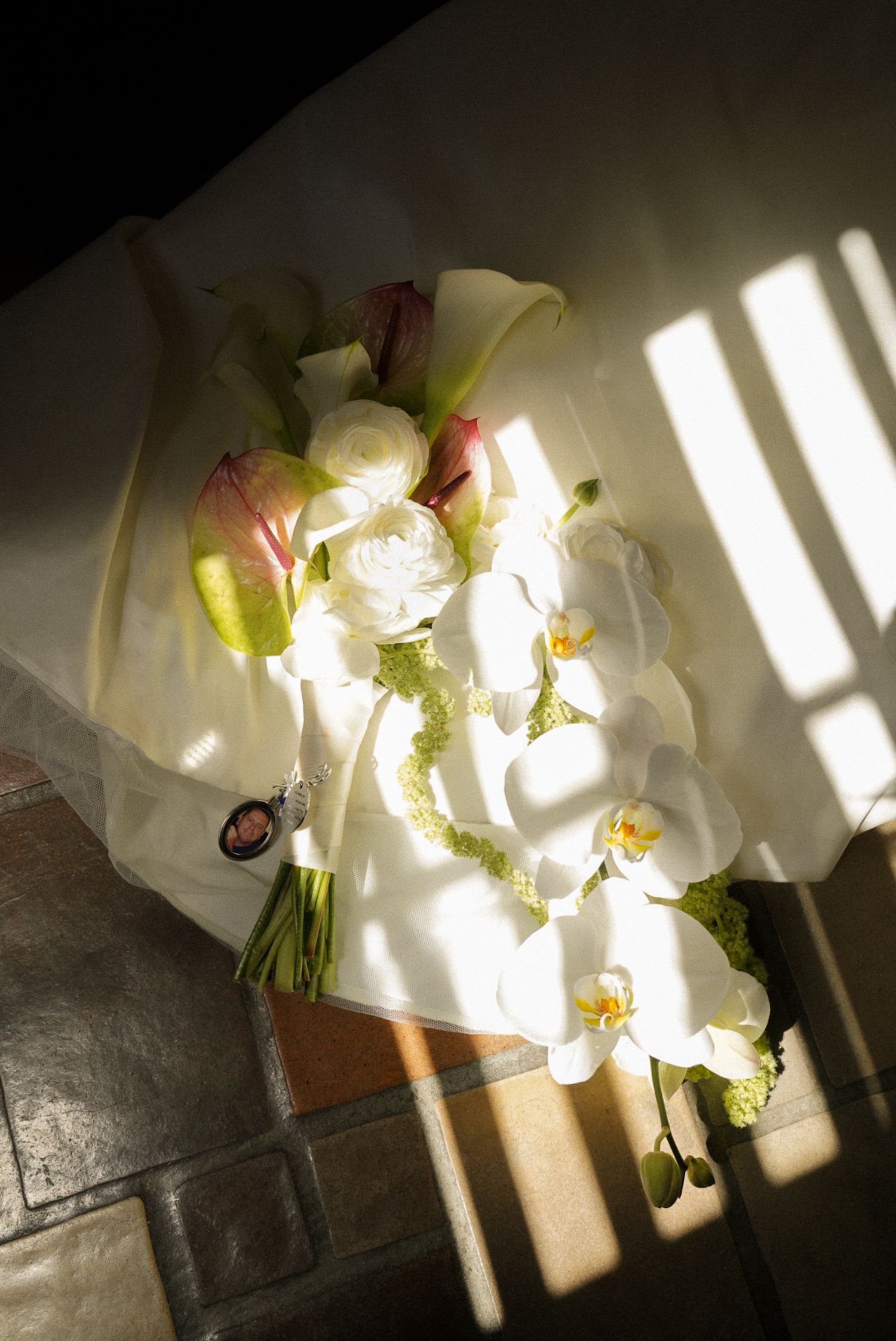Elegant bridal bouquet with white orchids, calla lilies, and pink tulips resting in sunlight on tiled steps.