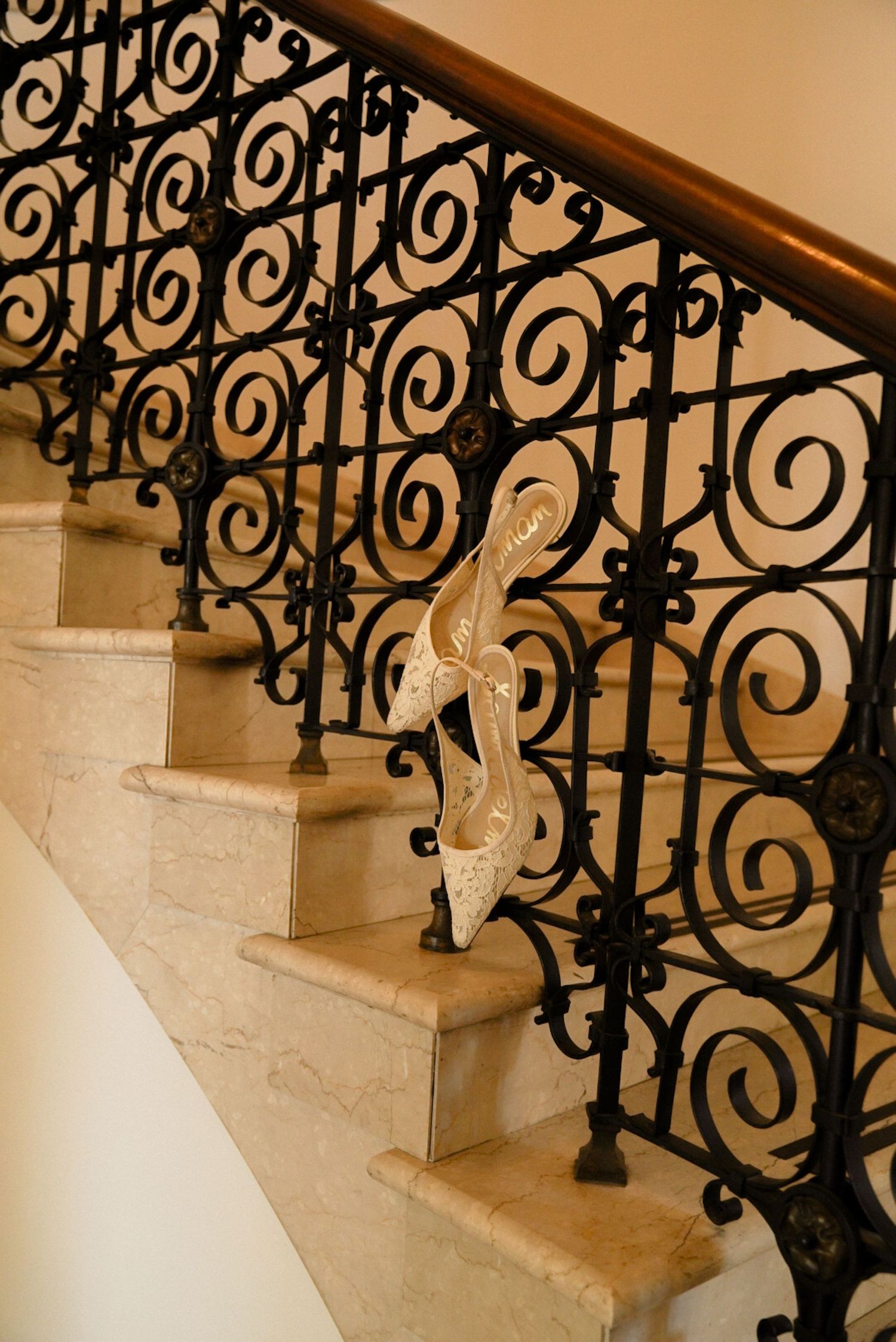 White bridal heels displayed on marble stairs with ornate black wrought iron railing.