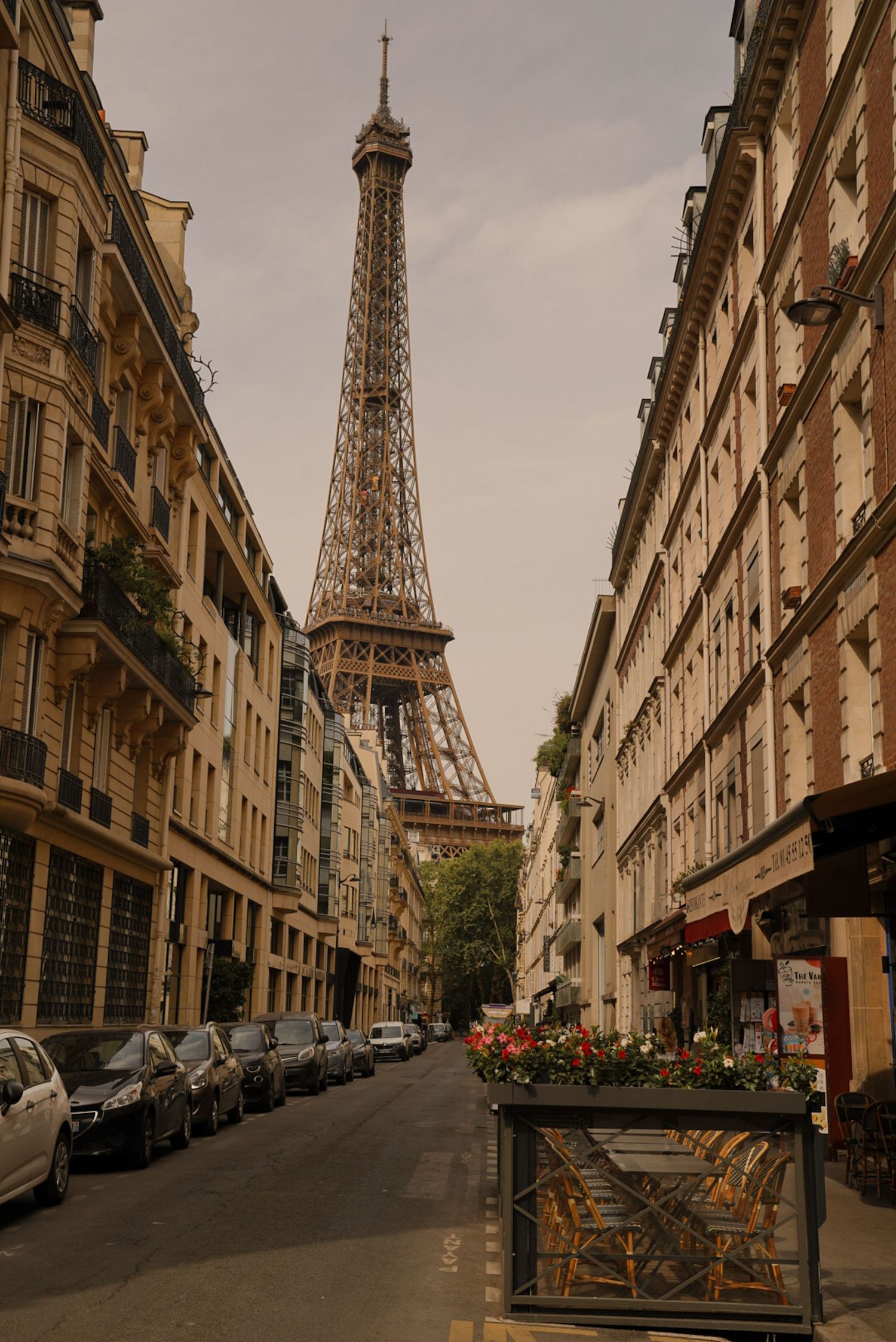 A charming Parisian street lined with classic Haussmann buildings leads to the iconic Eiffel Tower under a cloudy sky.