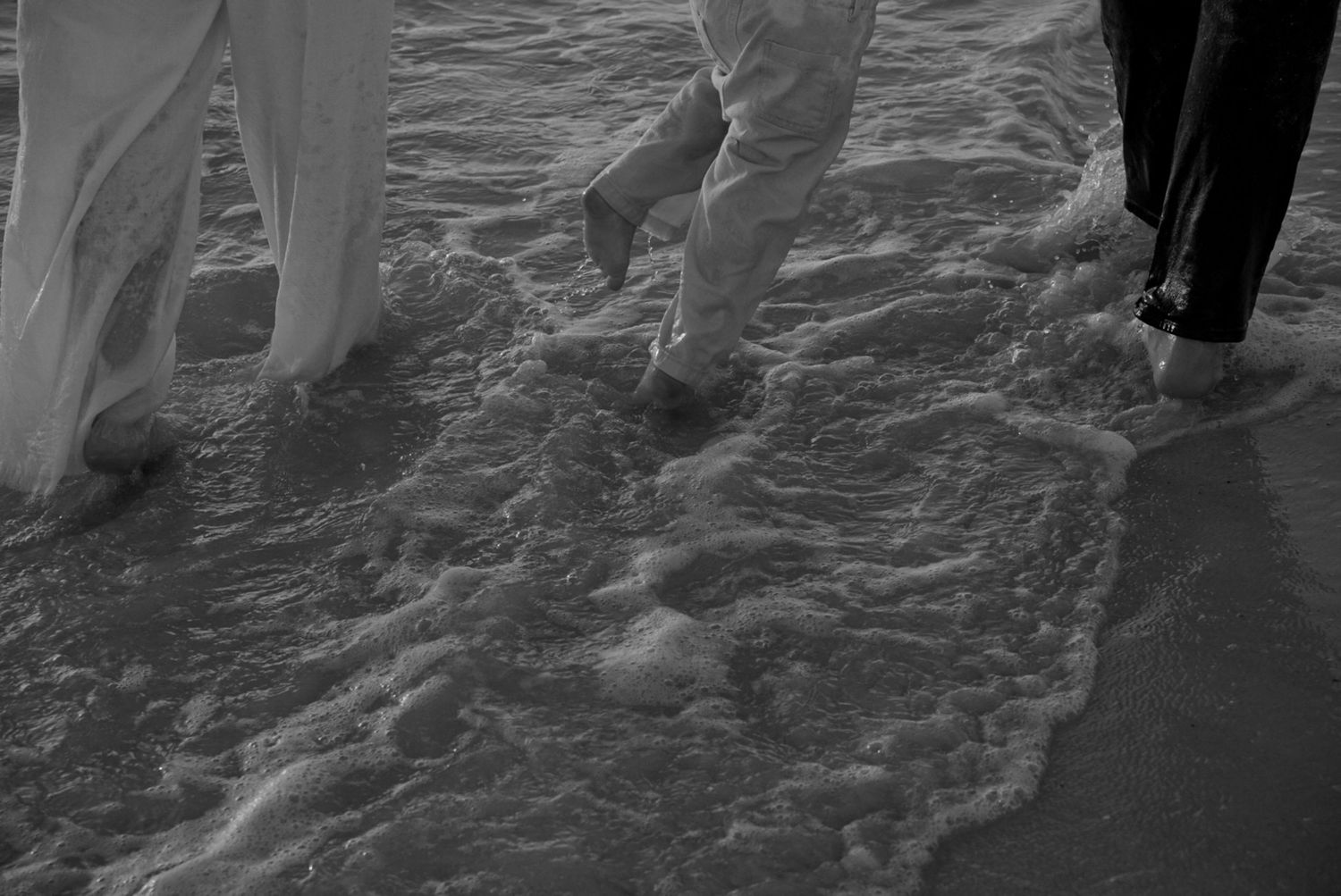 Couple walking along beach shoreline in black and white.