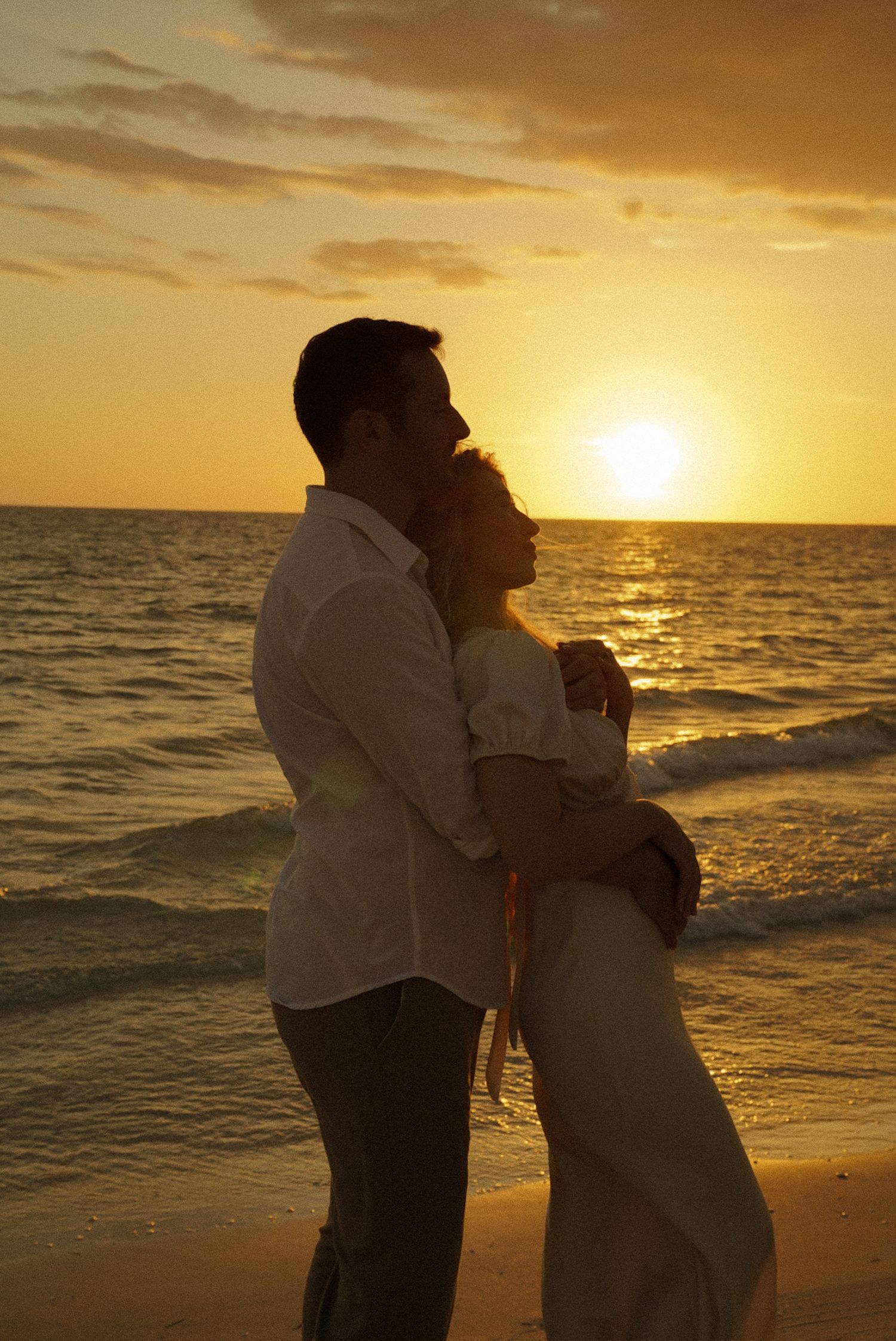 Romantic couple embracing on a tropical beach at golden sunset, waves gently lapping the shore behind them.