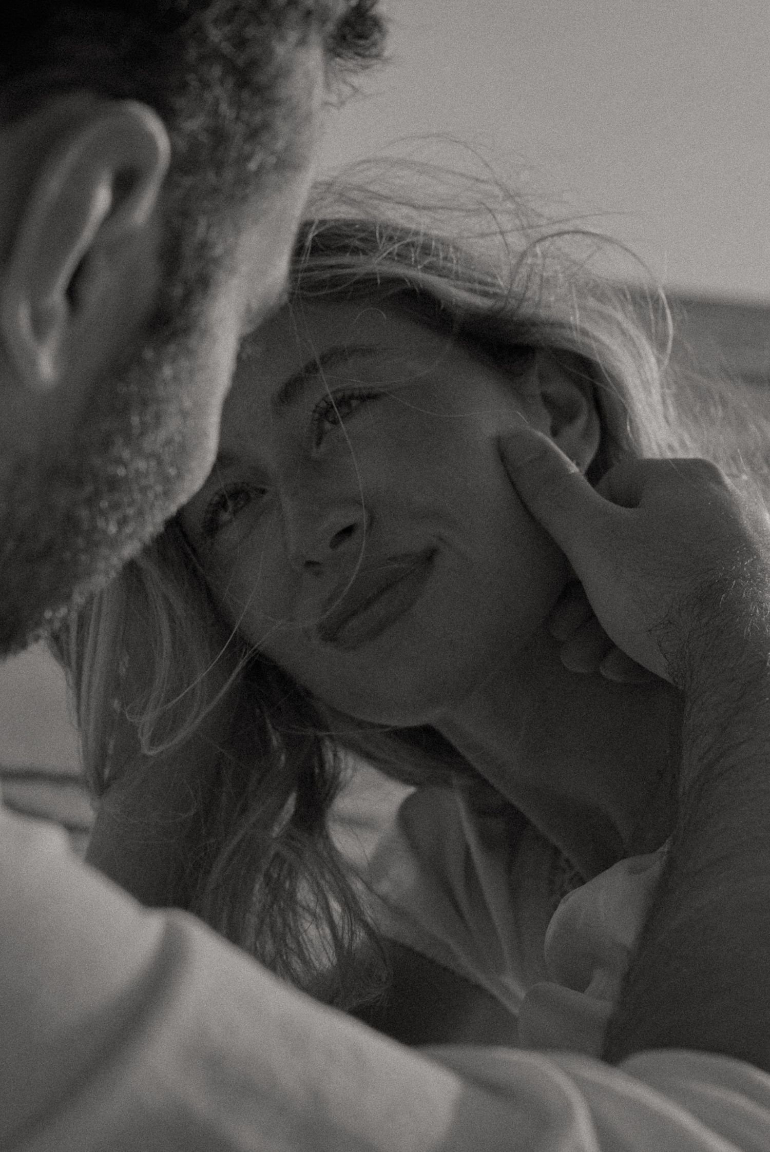 Black and white photo of a couple sharing an intimate moment, man gently cupping womans face as she smiles softly.