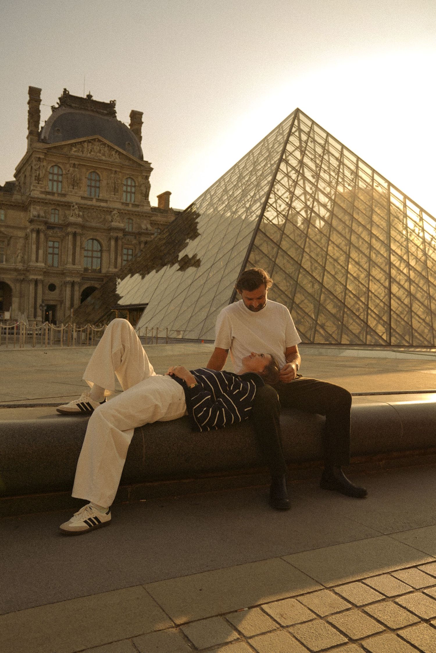 Couple relaxing by the Louvre Pyramid at golden hour in Paris, France.