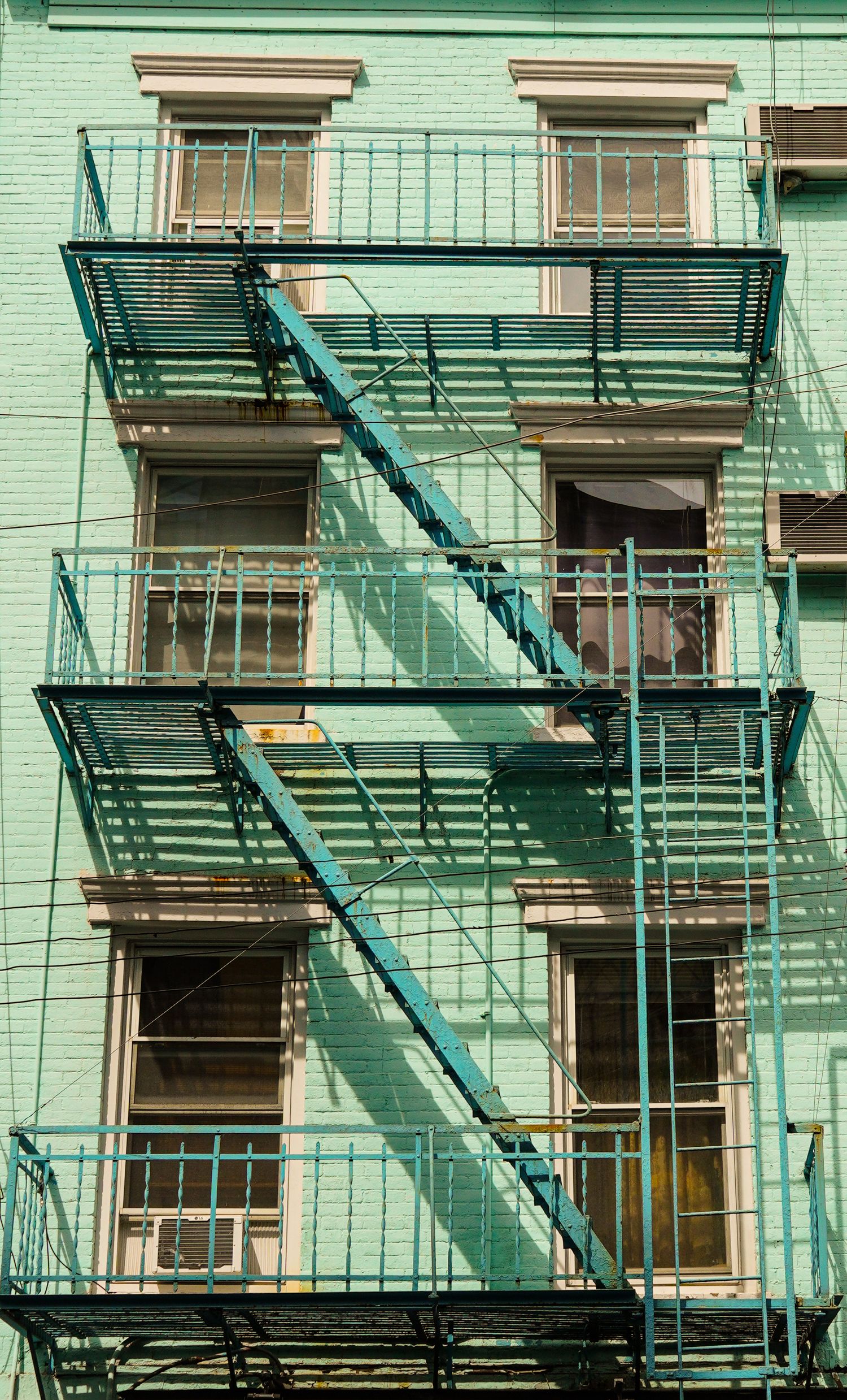 Mint green painted building facade with fire escapes and windows in an urban setting.