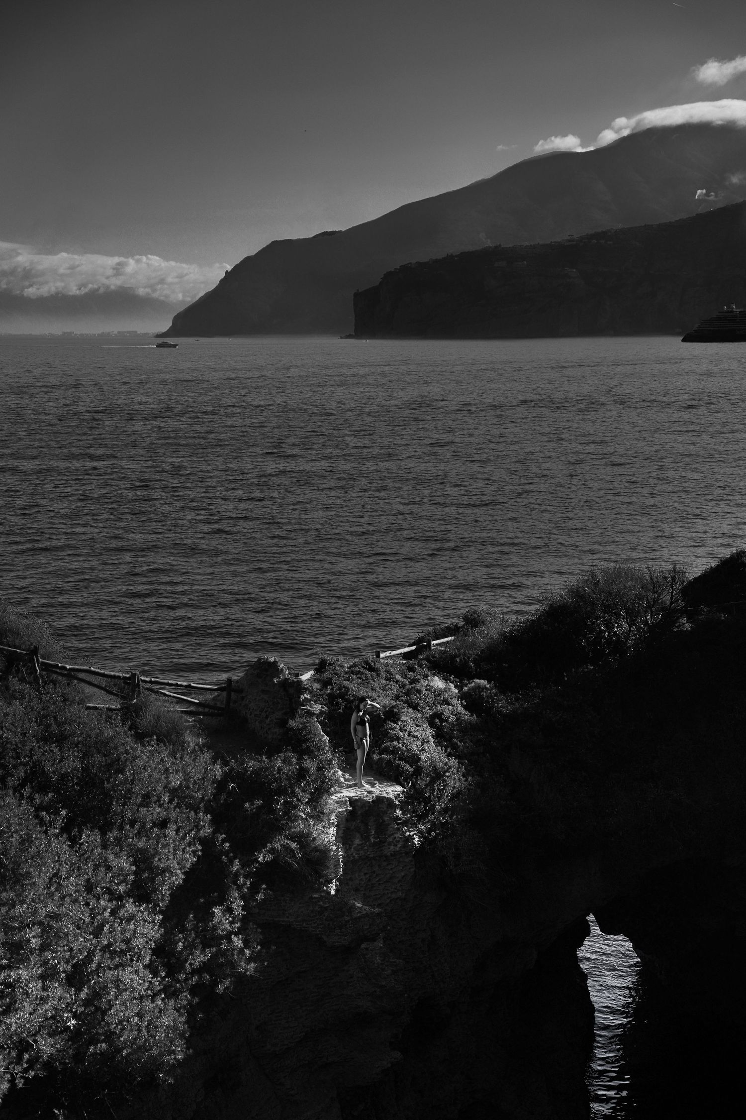 Dramatic black and white coastal landscape with rocky cliffs and dark waters stretching to the horizon.