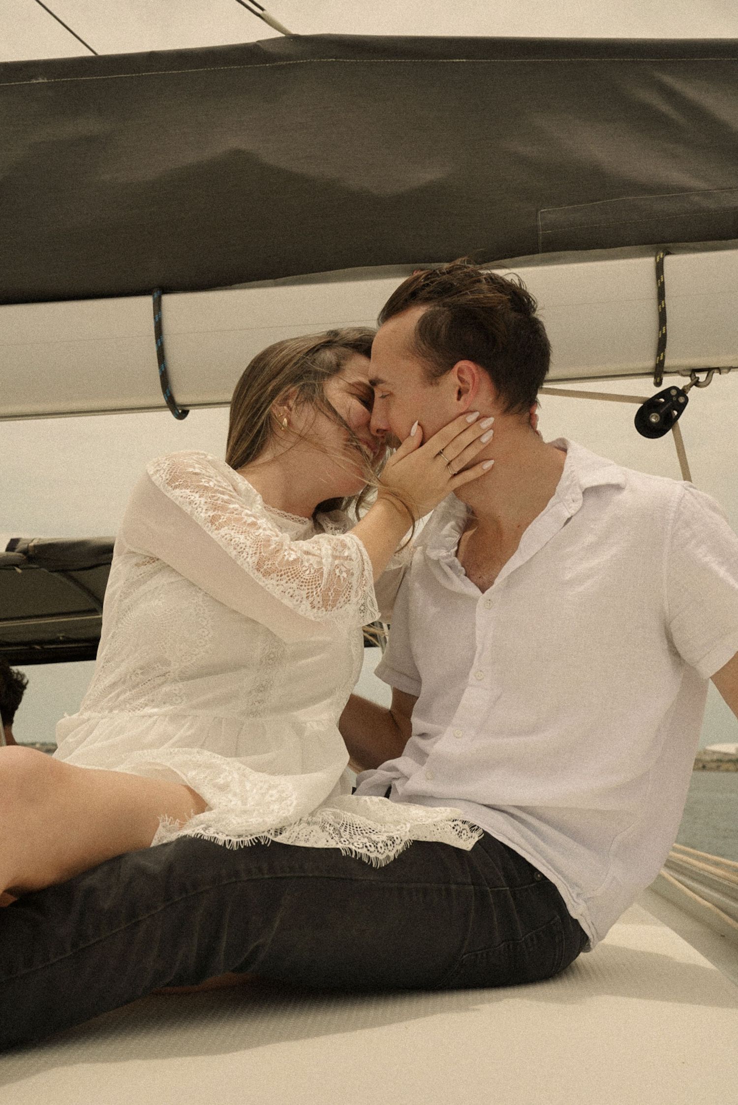 Romantic couple sharing a kiss on a sailboat deck, woman in white lace dress, man in white shirt.