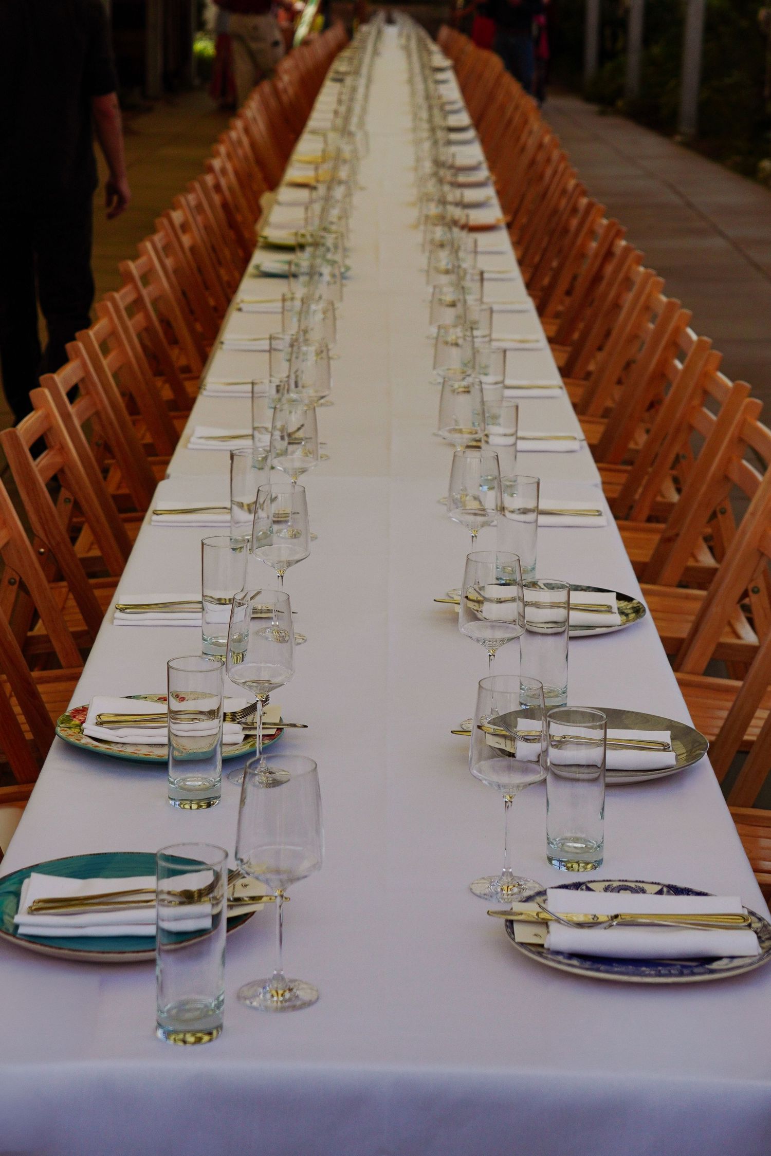 Long white banquet table set with elegant place settings and wooden chairs for a formal event.