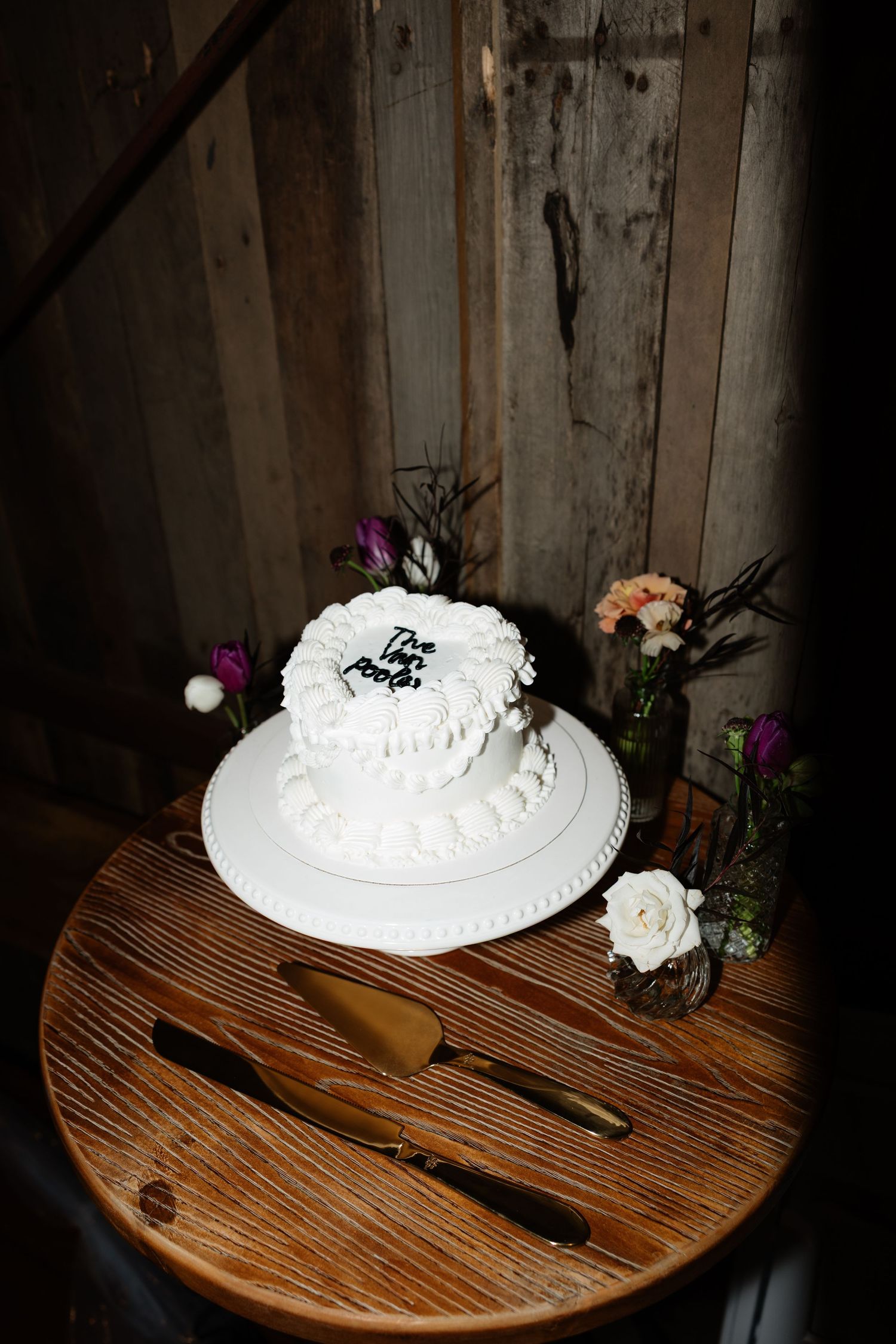Single-tier white wedding cake with floral decor displayed on rustic wooden table.
