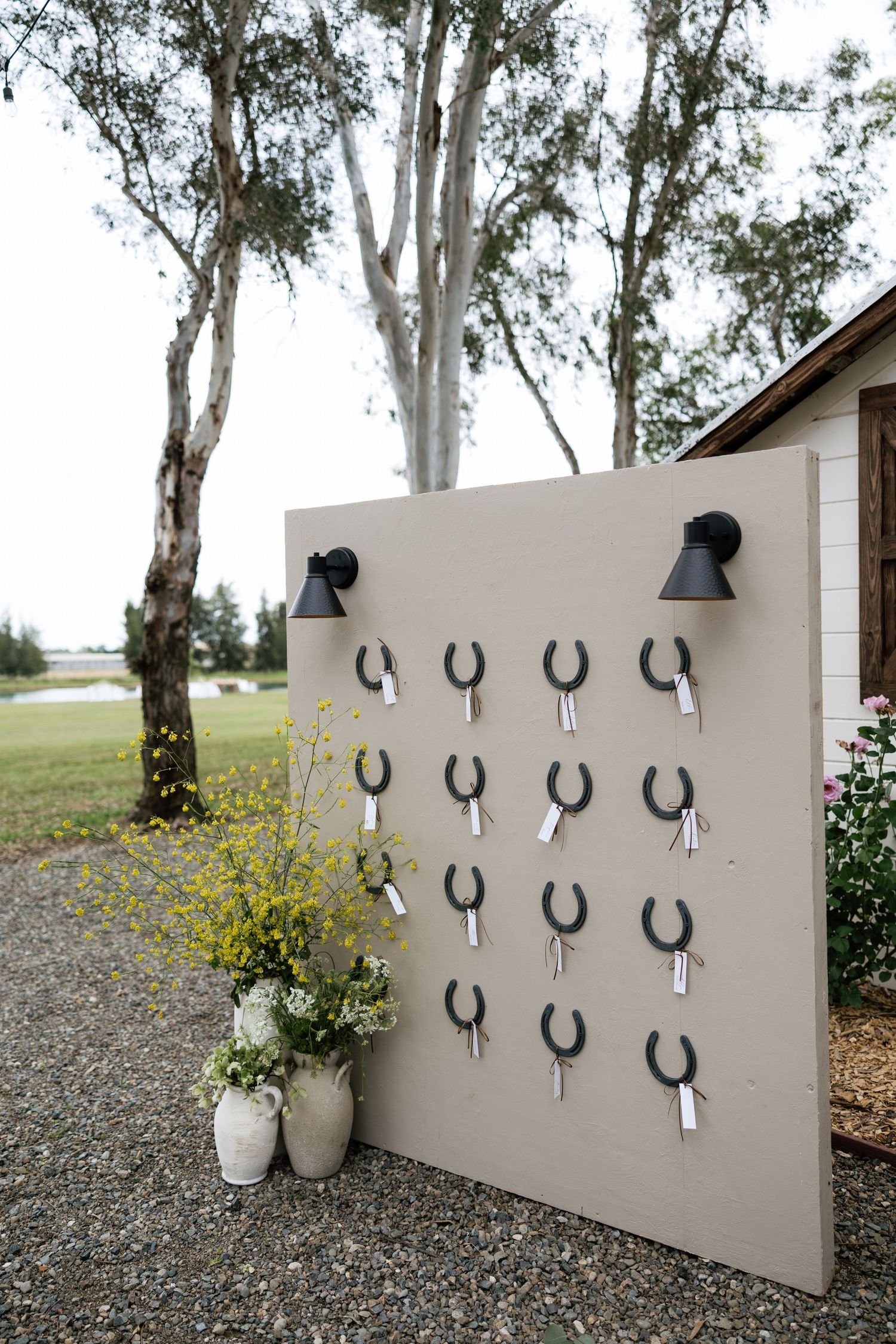 Outdoor wedding seating chart display with horseshoe hooks on a neutral board flanked by wall sconces.