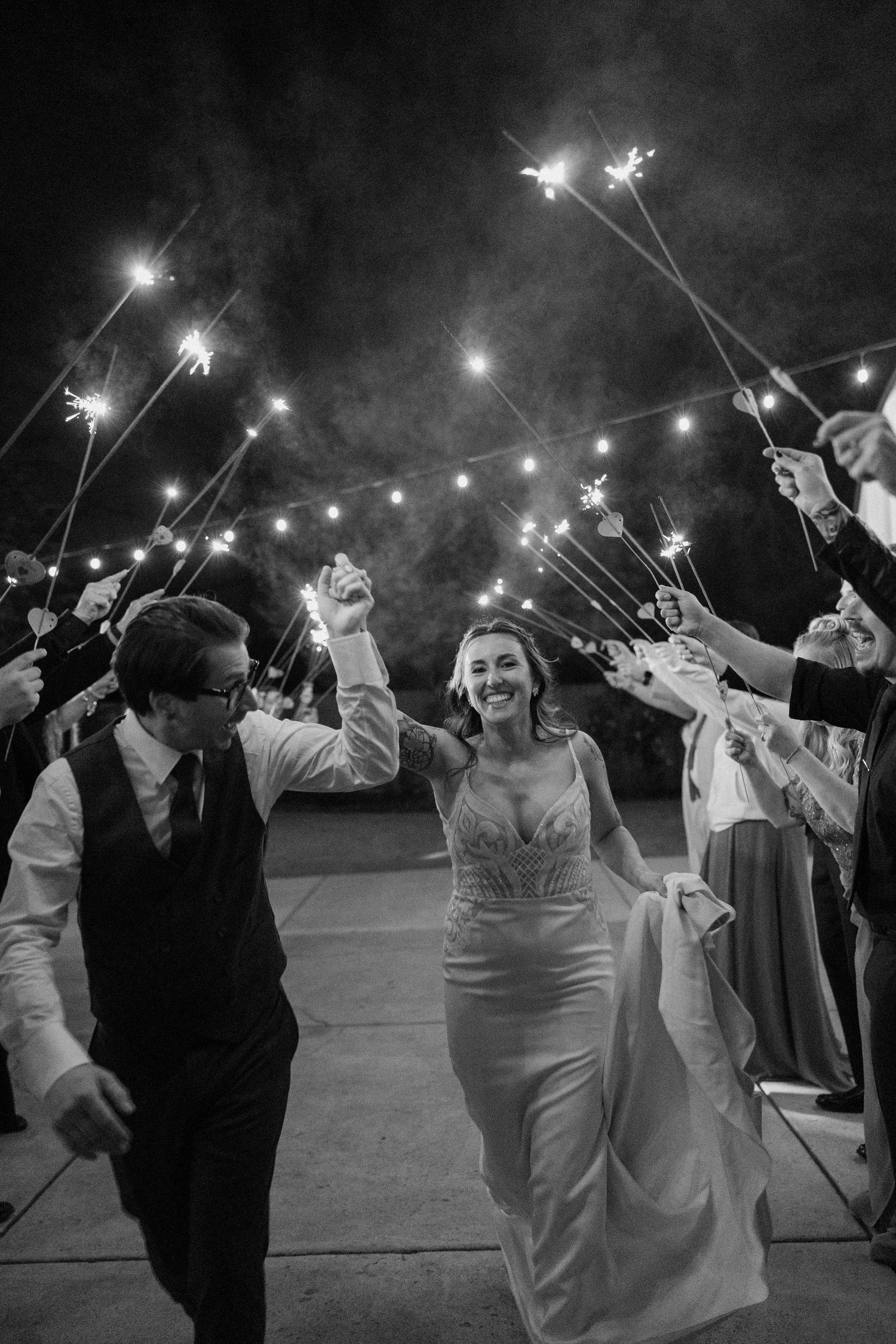Black and white photo of bride and groom walking through sparkler exit at night wedding reception.
