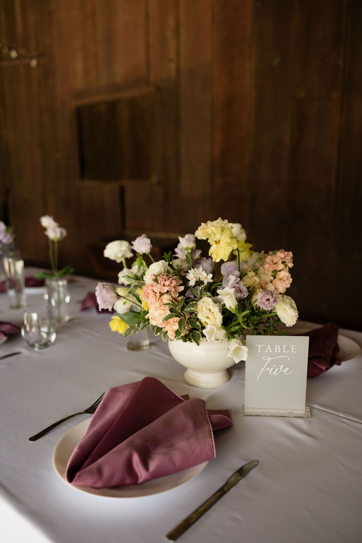Elegant wedding table setting with pastel floral centerpiece, mauve napkins, and Table Five card.